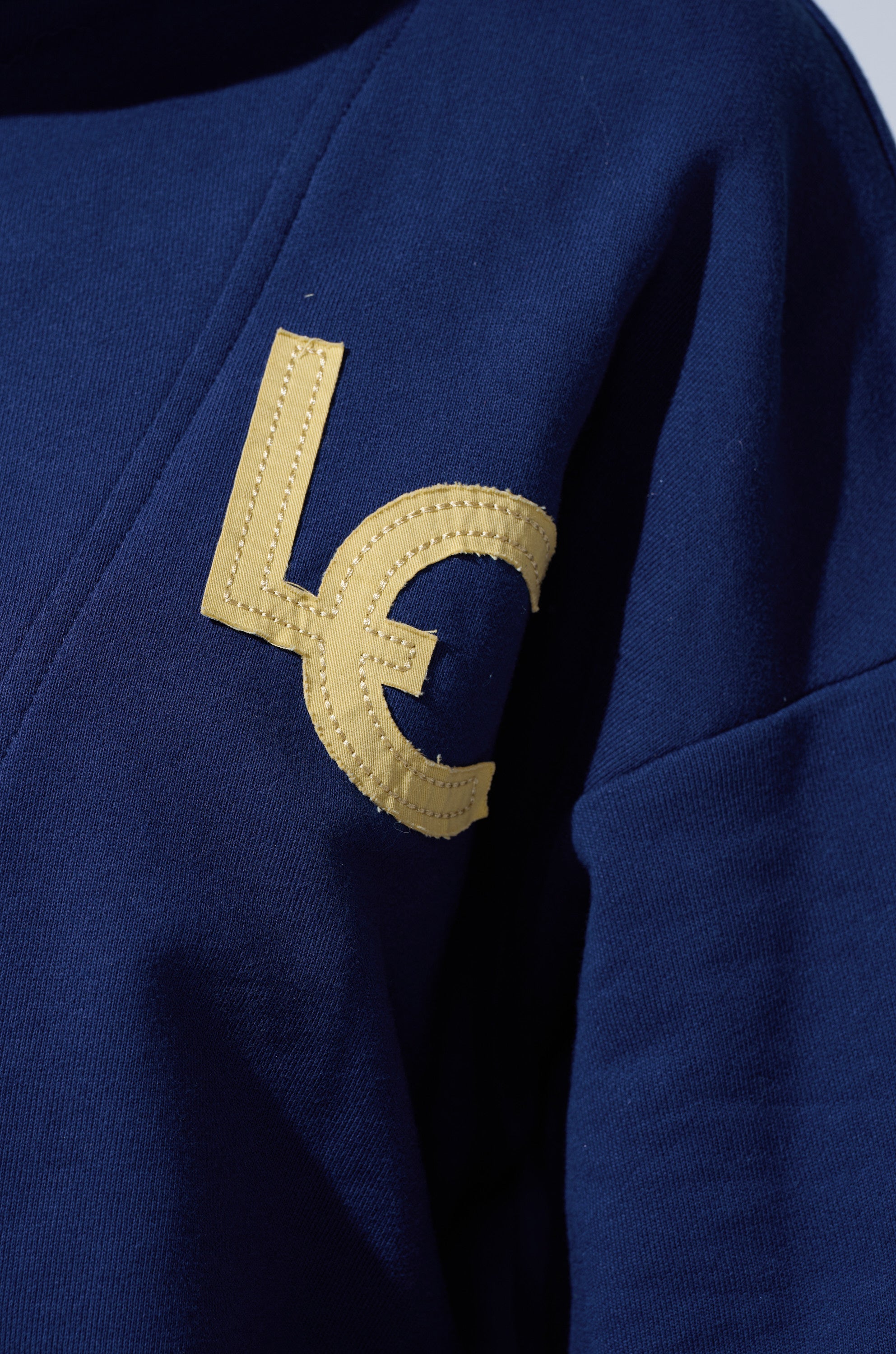 Close-up of the CITY LOVER OVERSIZED SWEATSHIRT in navy blue, crafted from a cozy cotton blend with a yellow "L" and "C" patch on the chest—ideal for fans of NYC lovers club style.