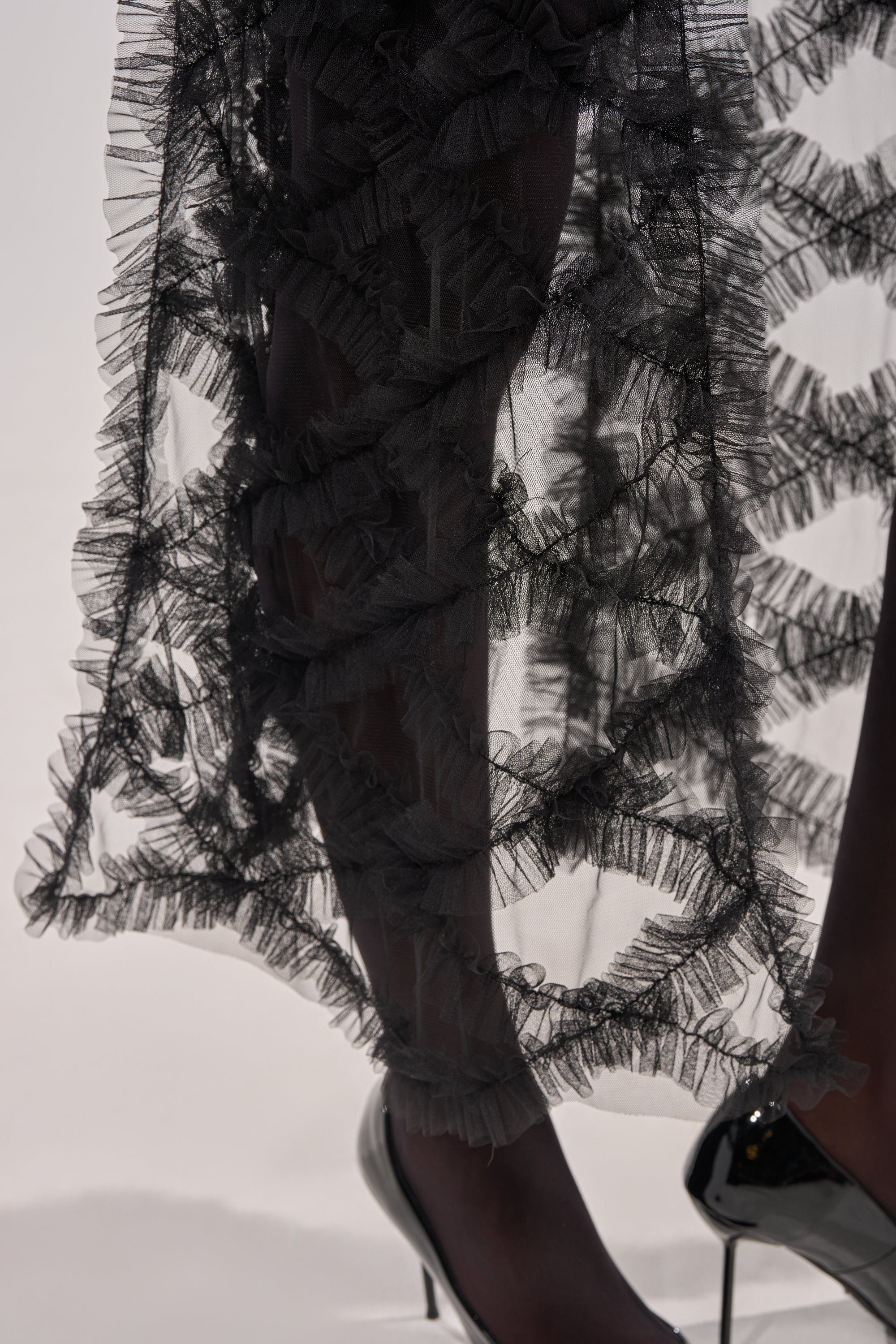 Close-up of a person wearing the BRING ON THE DRAMA BLOUSE, featuring sheer black ruffles and textured wavy layers, styled for a fashion-forward festival look against a minimal white background. 9