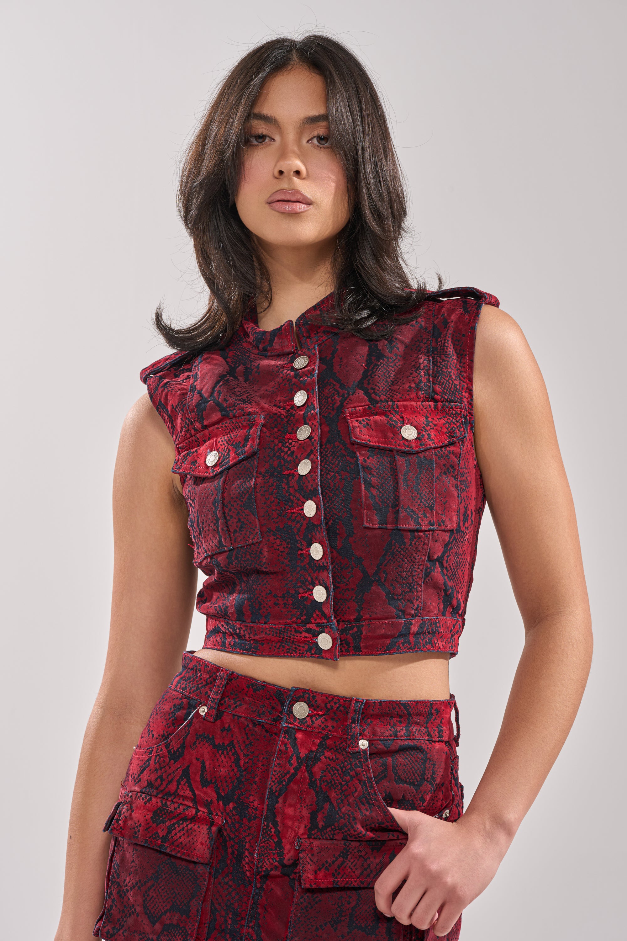 A woman with medium-length dark hair wears the FLOATING IN BETWEEN SNAKE BUTTON DOWN crop top and matching high-waisted pants, posing against a plain light gray background. 0