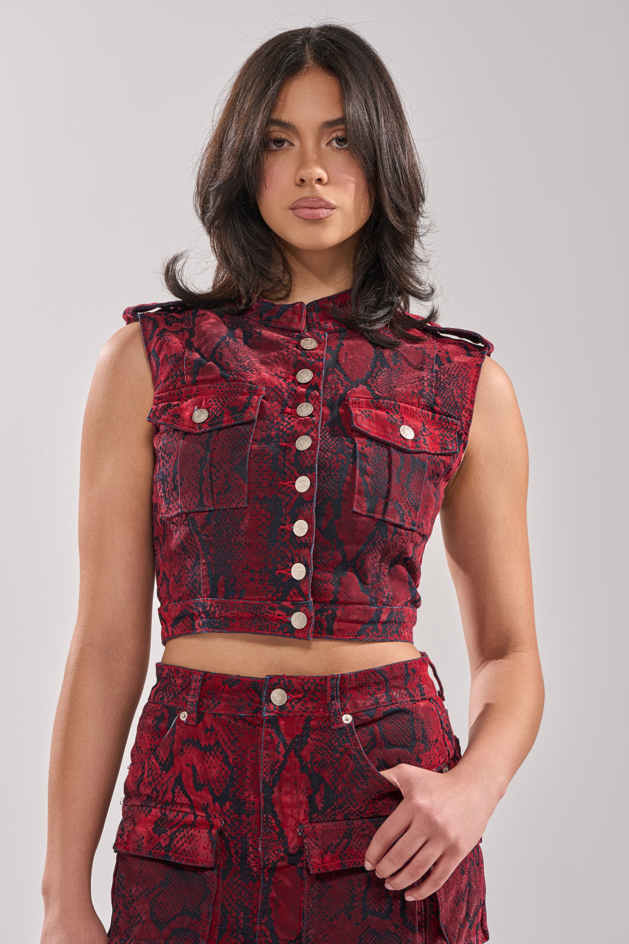 A woman with medium-length dark hair wears the FLOATING IN BETWEEN SNAKE BUTTON DOWN crop top and matching high-waisted skirt, posing against a plain light gray background. 1