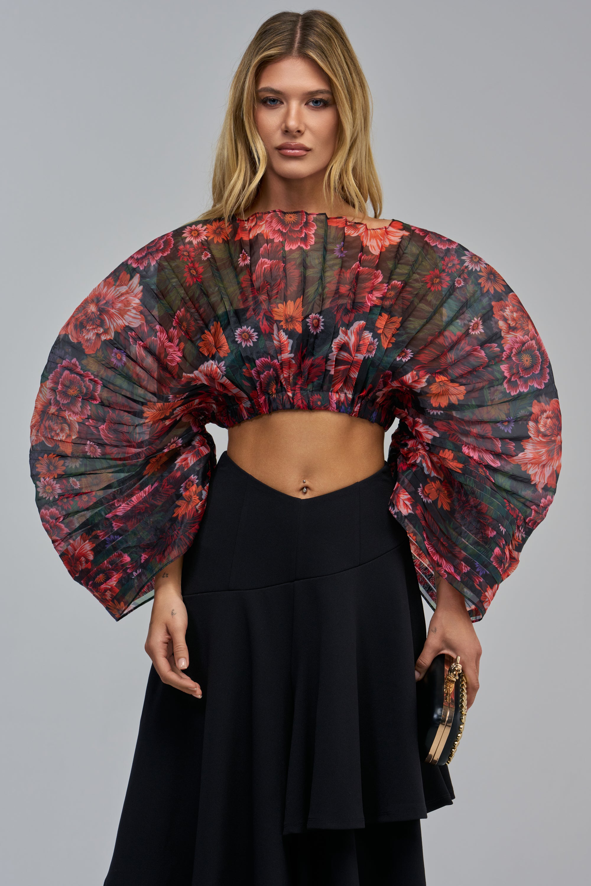 The LYSSA PLEATED BLOUSE, a cropped, pleated floral top with voluminous sleeves, worn with a black high-waisted skirt.