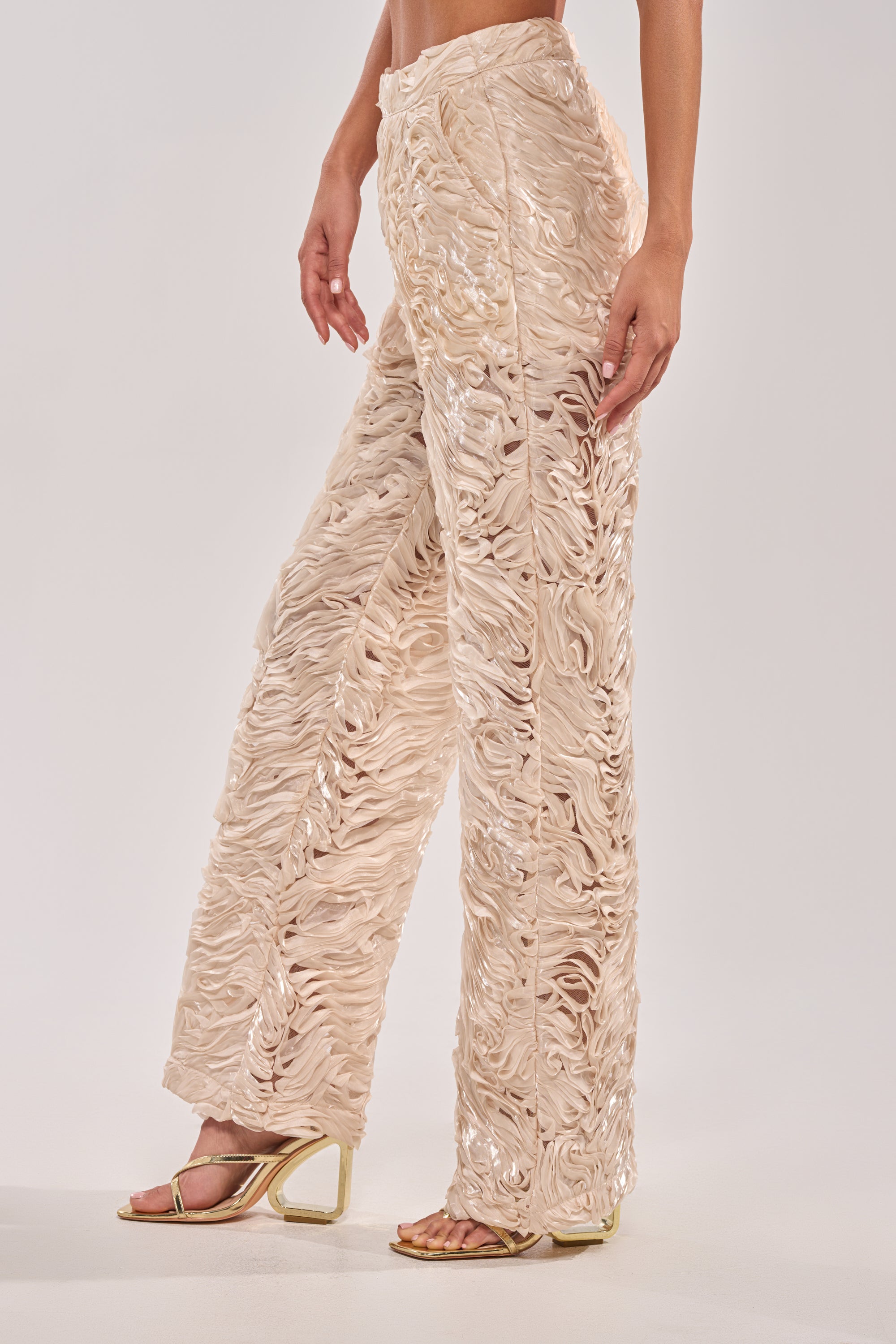 A person wears the WAVY AND COOL TROUSER—ivory, wide-leg bridal pants in light beige semi-sheer fabric—paired with gold heeled sandals, standing against a plain background.
