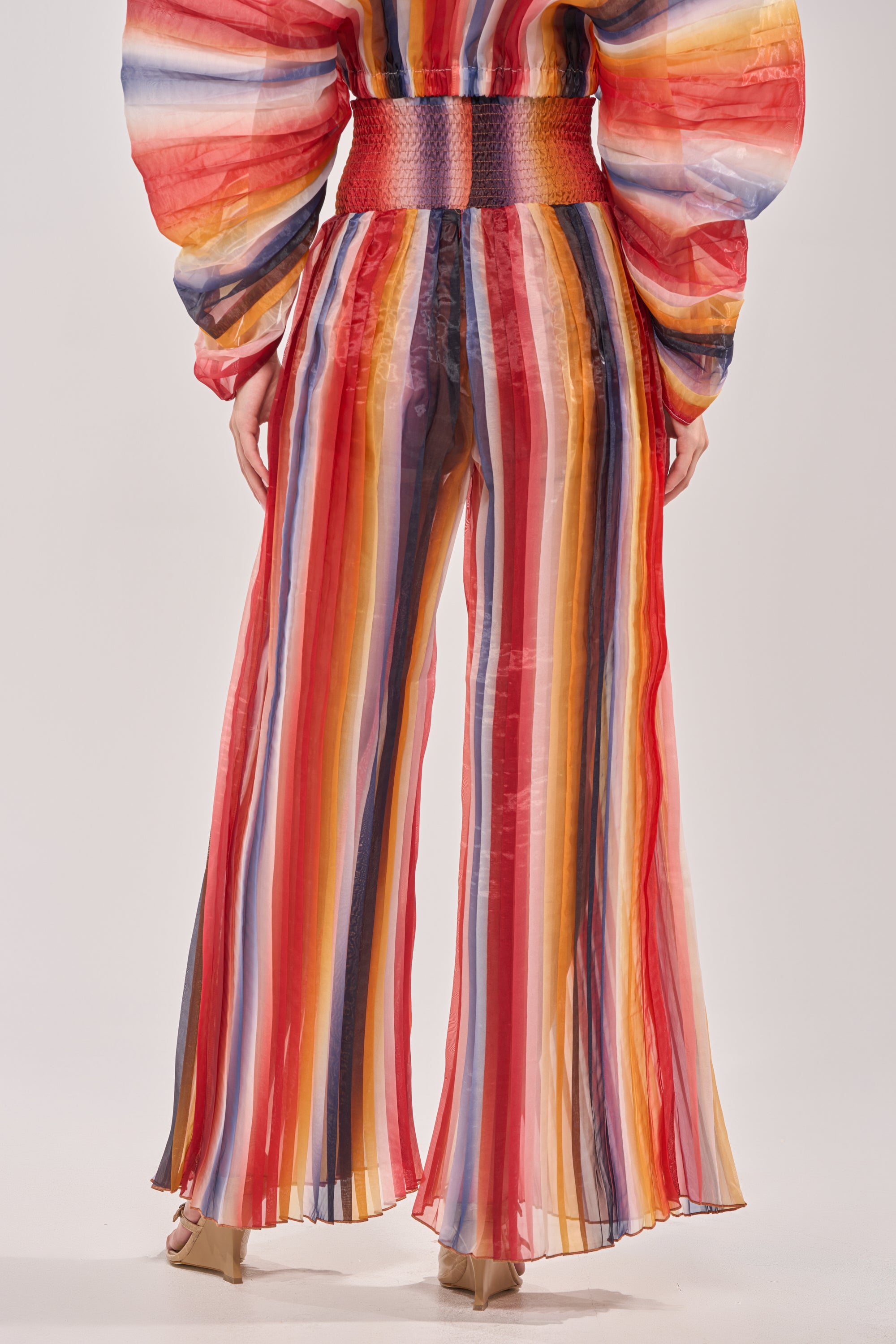 Someone wearing the FANNED OUT CHIFFON PANT—a pair of colorful, vertically striped wide-leg pants—with a matching billowy-sleeved top, shown from the back against a plain background.