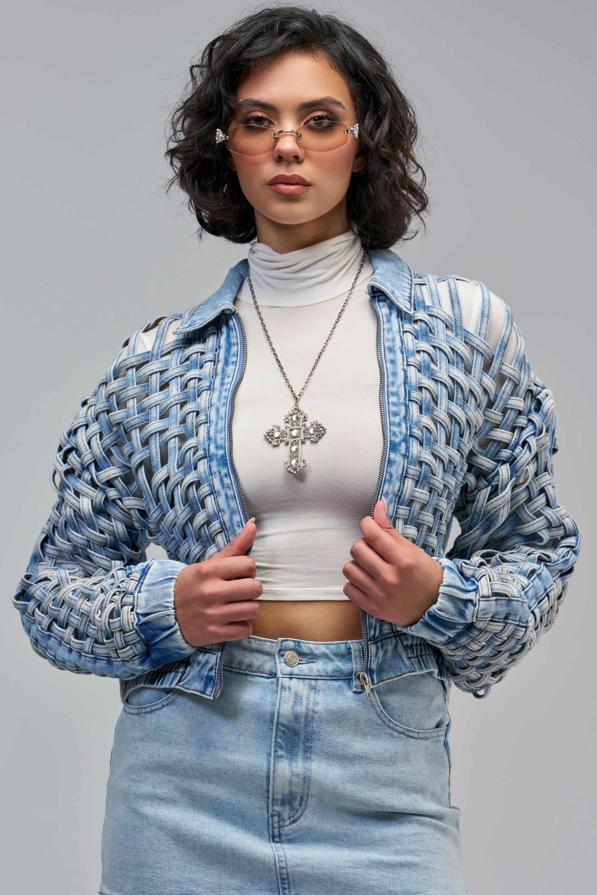 A person wears a light wash, lattice-pattern BOP N WEAVE DENIM JACKET over a white turtleneck and a cross necklace.