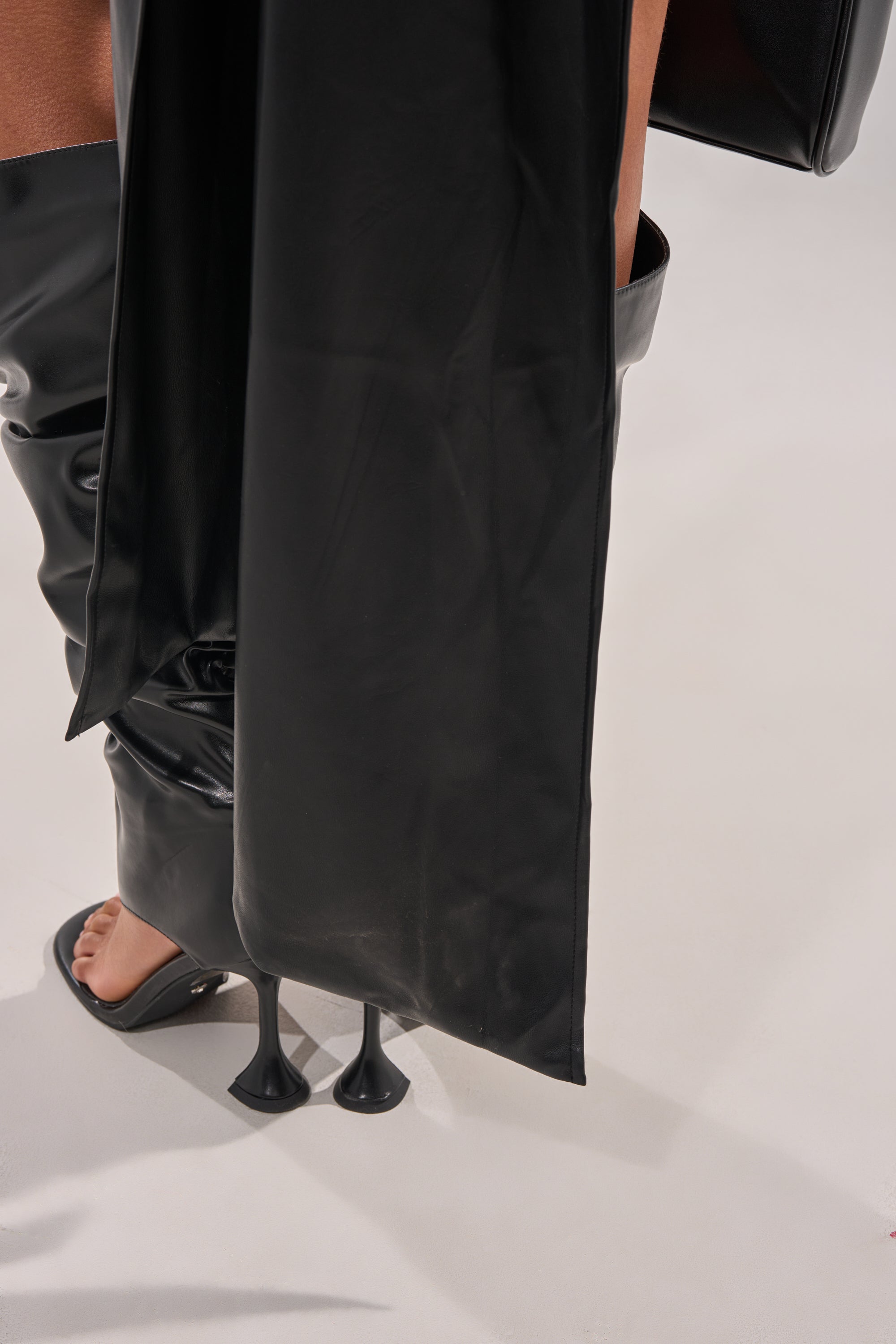 A person stands on a light floor wearing the BABY GIRL FAUX LEATHER BLOUSE, paired with black open-toe high-heeled boots. 8