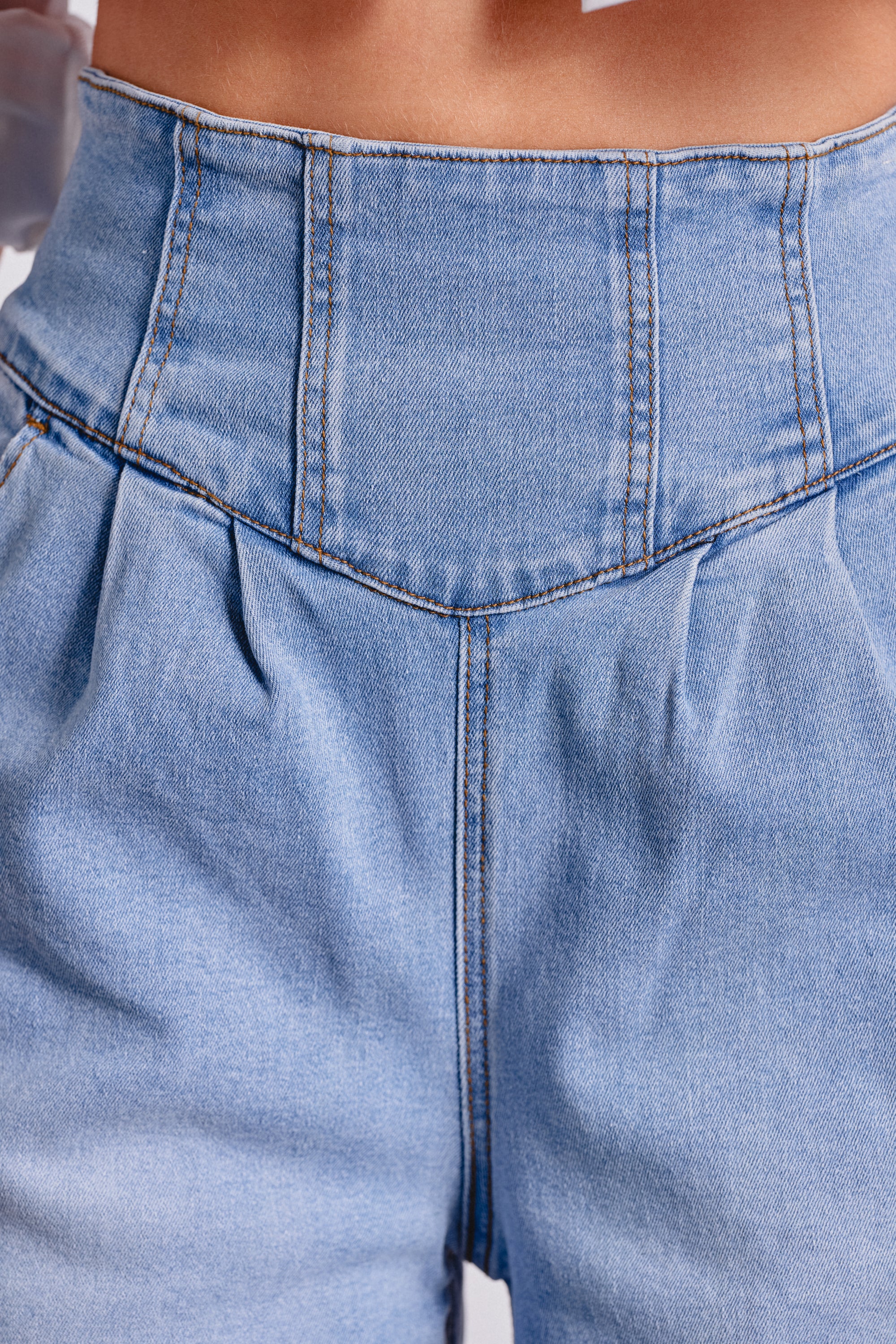 A close-up of a person wearing the JENNY WIDE LEG DENIM, featuring high-waisted, light blue washed denim with visible seams and a sculpted waistband accented by pleats. 5