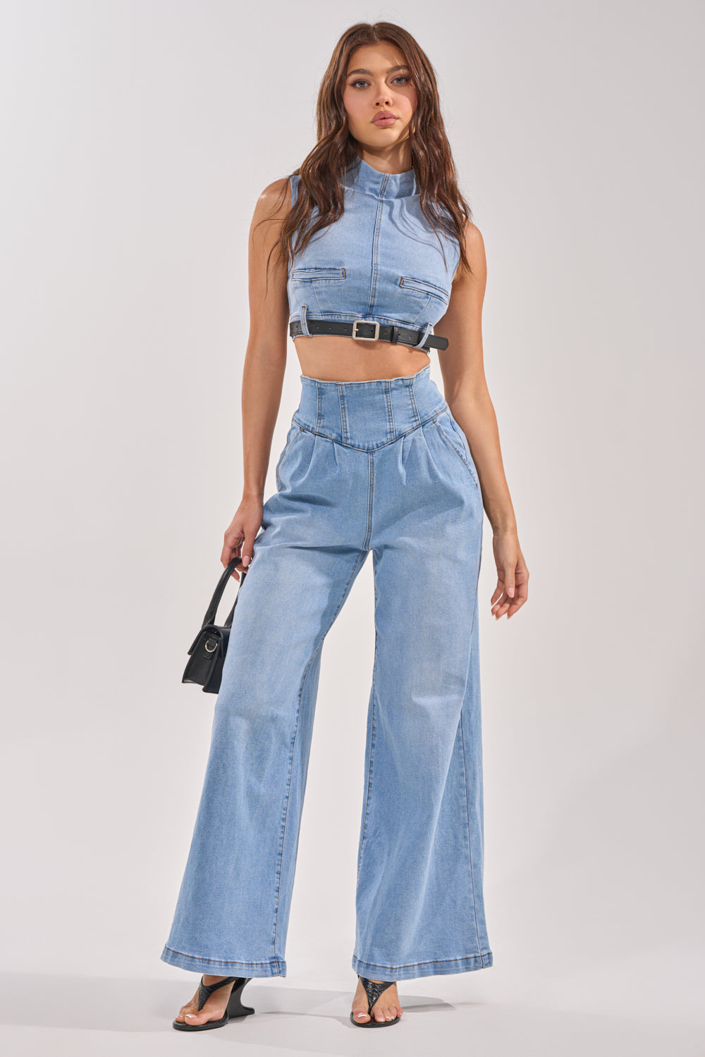 A woman stands confidently in the JENNY DENIM BLOUSE, paired with high-waisted wide-leg jeans. She carries a small black handbag and wears black heeled sandals, posing against a plain light background for an effortless streetwear look. 8