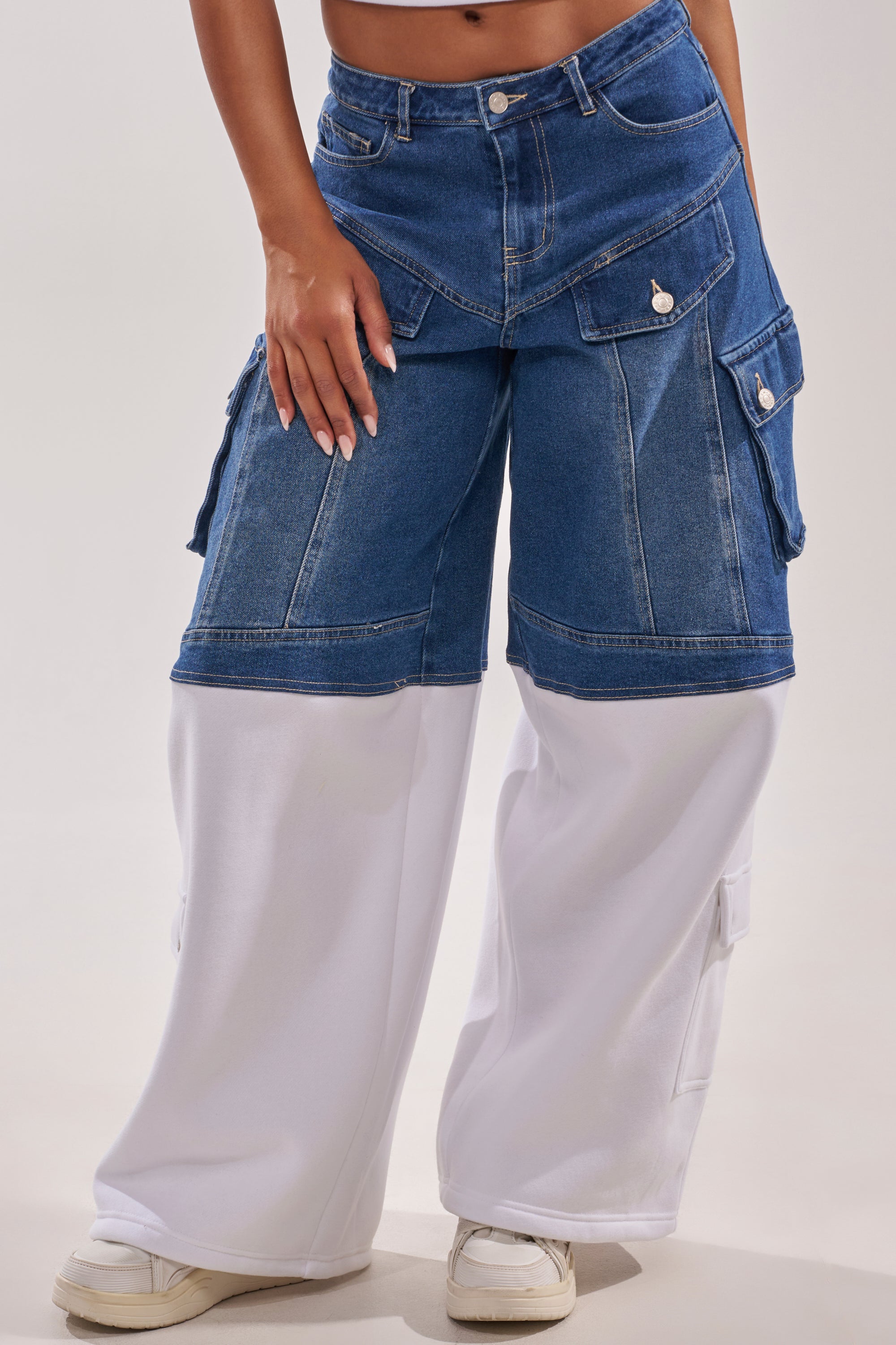 A person is seen from the waist down wearing THIS IS EVERYTHING YOU SEE RELAXED DENIM wide-leg streetwear pants with blue upper and white lower fabric, cargo pockets, and white sneakers. 1