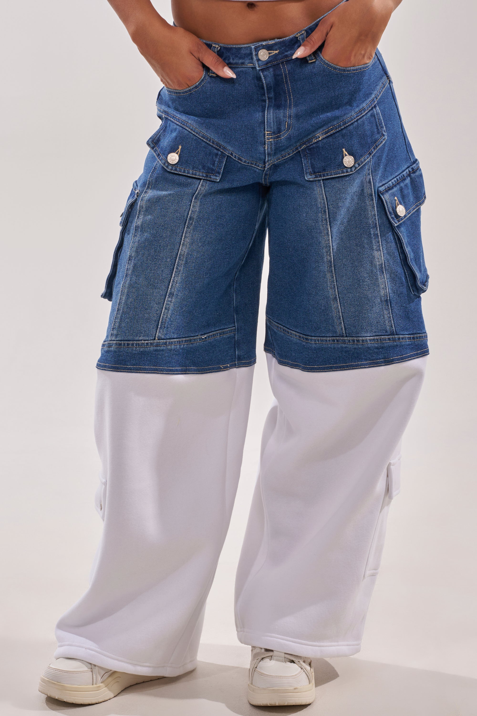 Wearing the THIS IS EVERYTHING YOU SEE RELAXED DENIM—wide-leg cargo shorts layered over white fabric—with white sneakers, hands in pockets, only the lower half of the body is visible. 2