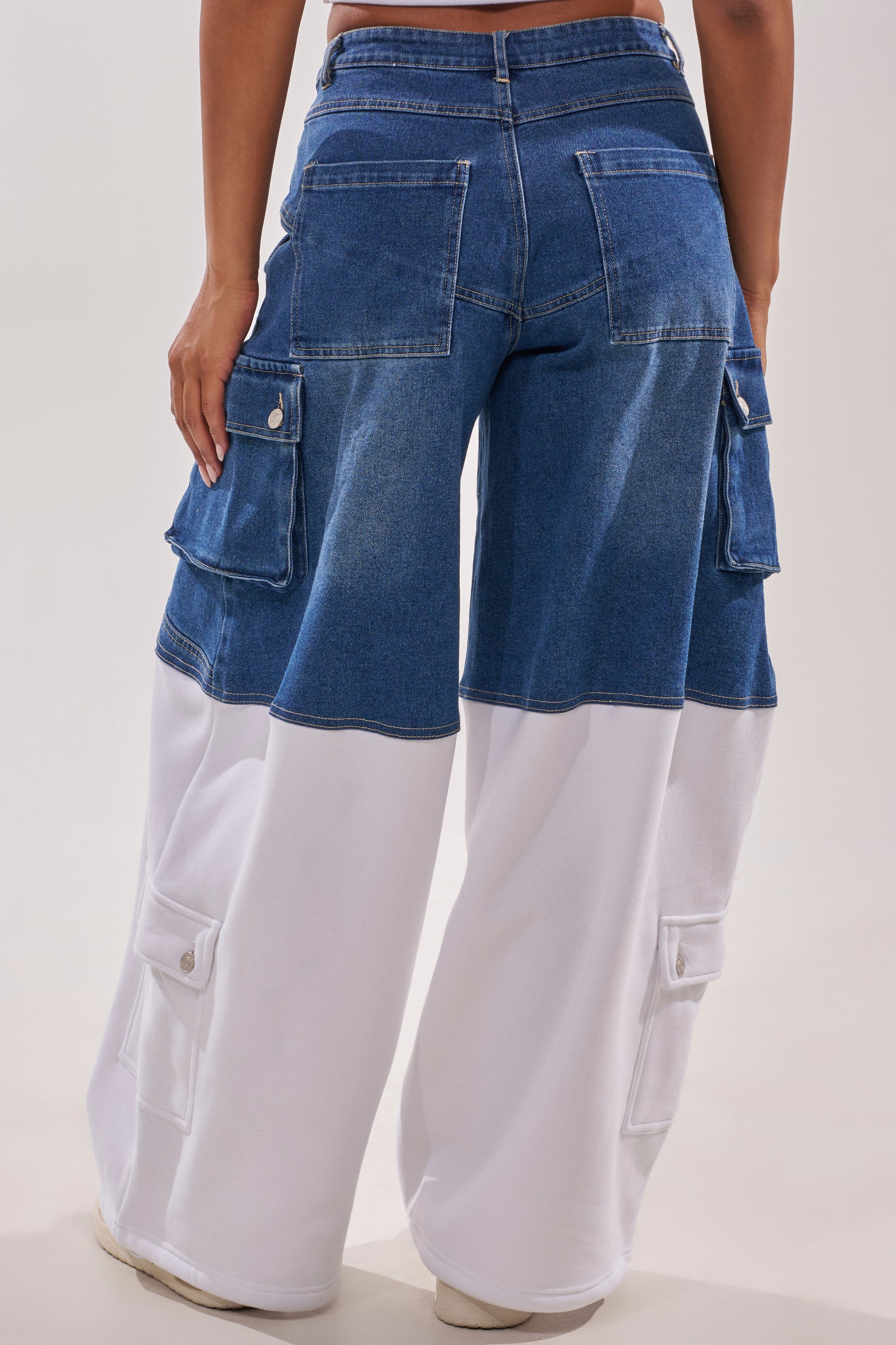 Someone is wearing the THIS IS EVERYTHING YOU SEE RELAXED DENIM: wide-leg denim streetwear pants with a blue upper, white lower fabric, and cargo pockets on sides and back, standing with their back to the camera. 4