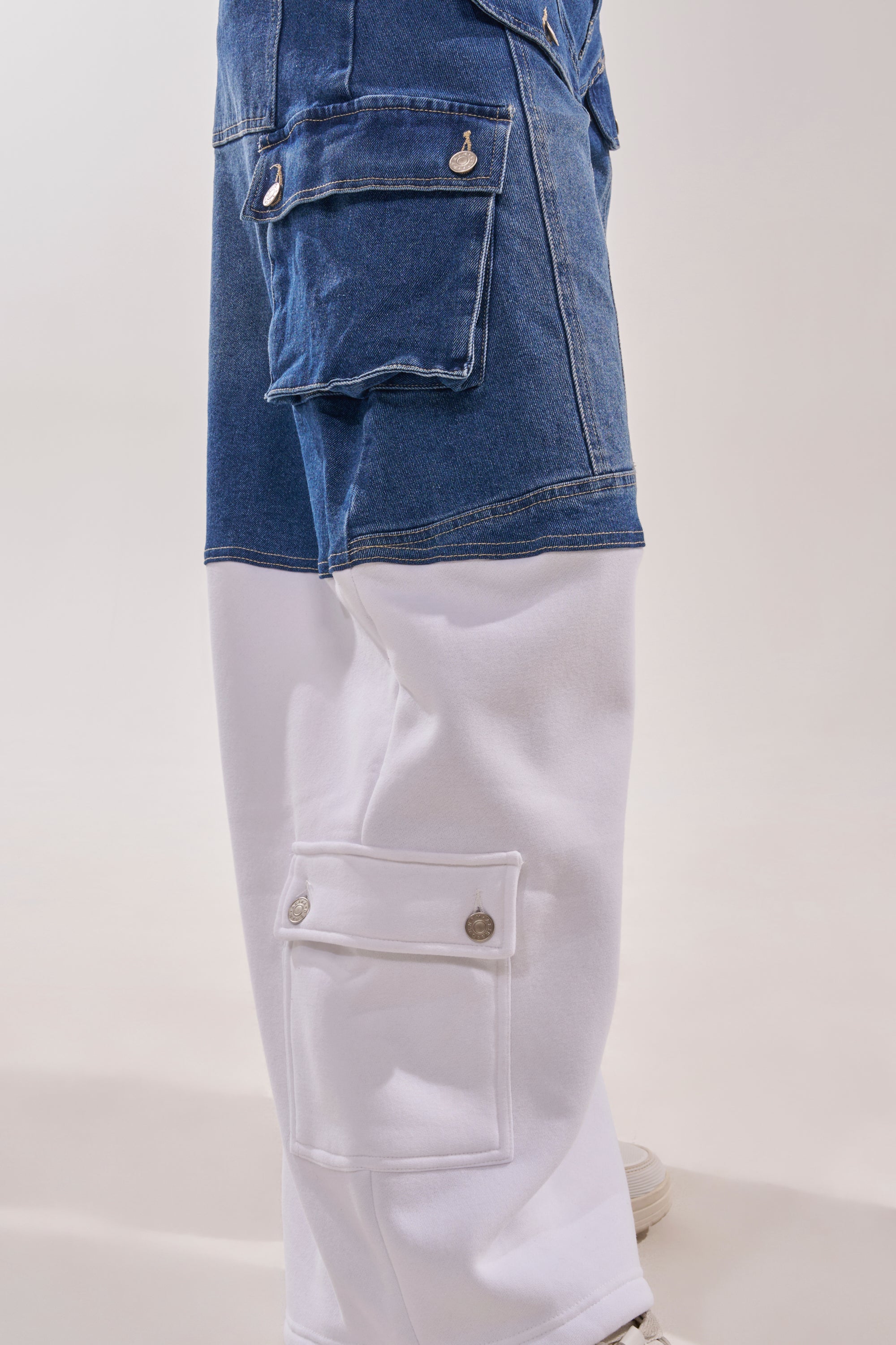 A close-up side view of a person wearing the THIS IS EVERYTHING YOU SEE RELAXED DENIM: two-tone cargo jeans with a blue denim upper, white lower section, wide-leg fit, large flap pockets, and silver buttons. 7