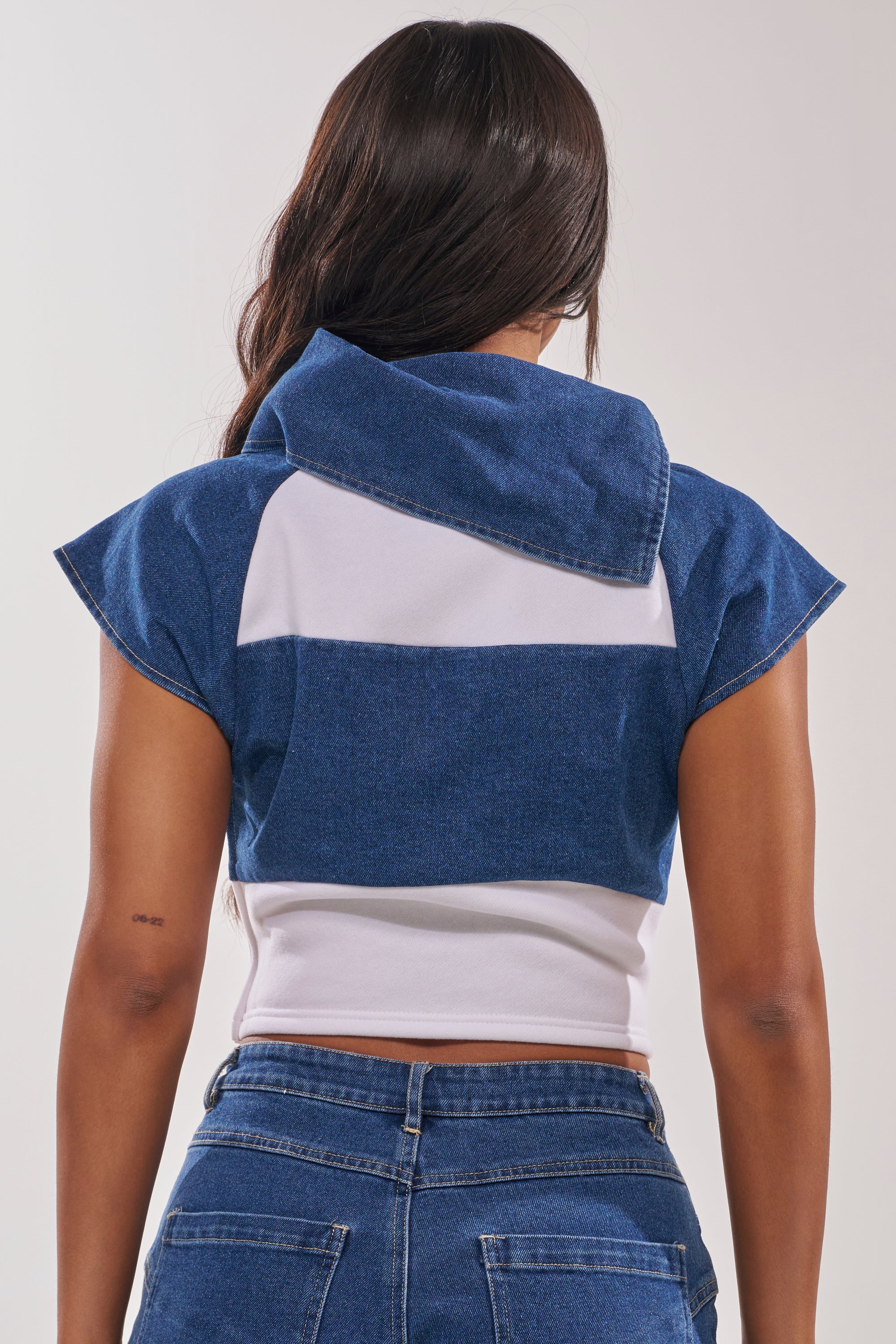 A woman with long dark hair is seen from the back wearing the THIS IS EVERYTHING YOU SEE DENIM BLOUSE, a cropped fitted top with an oversized collar, paired with high-waisted blue jeans. 5