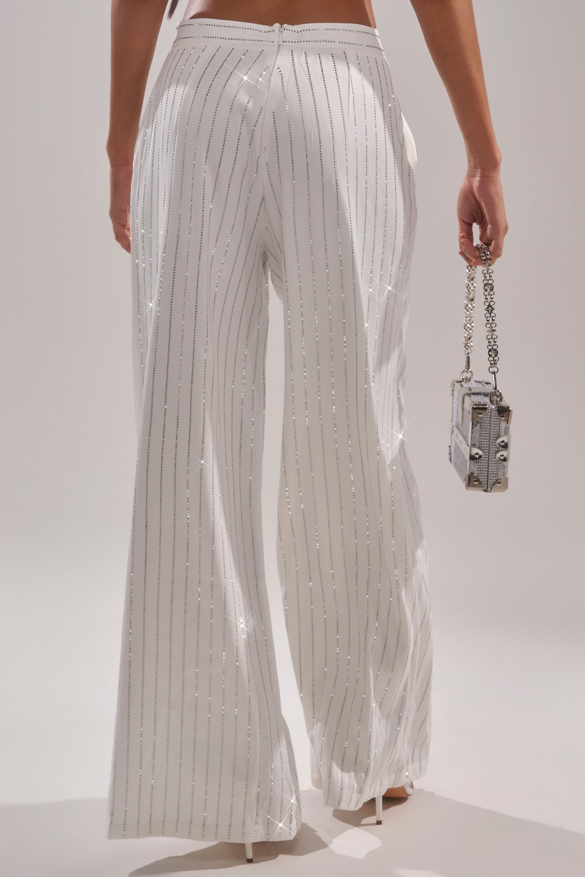 Rocking the PRINCESS TREATMENT RHINESTONE WIDE LEG PANT—high-waisted, sparkling with vertical silver stripes—paired with a chic small silver chain-strap purse, shown from behind waist down for a glam look. 4