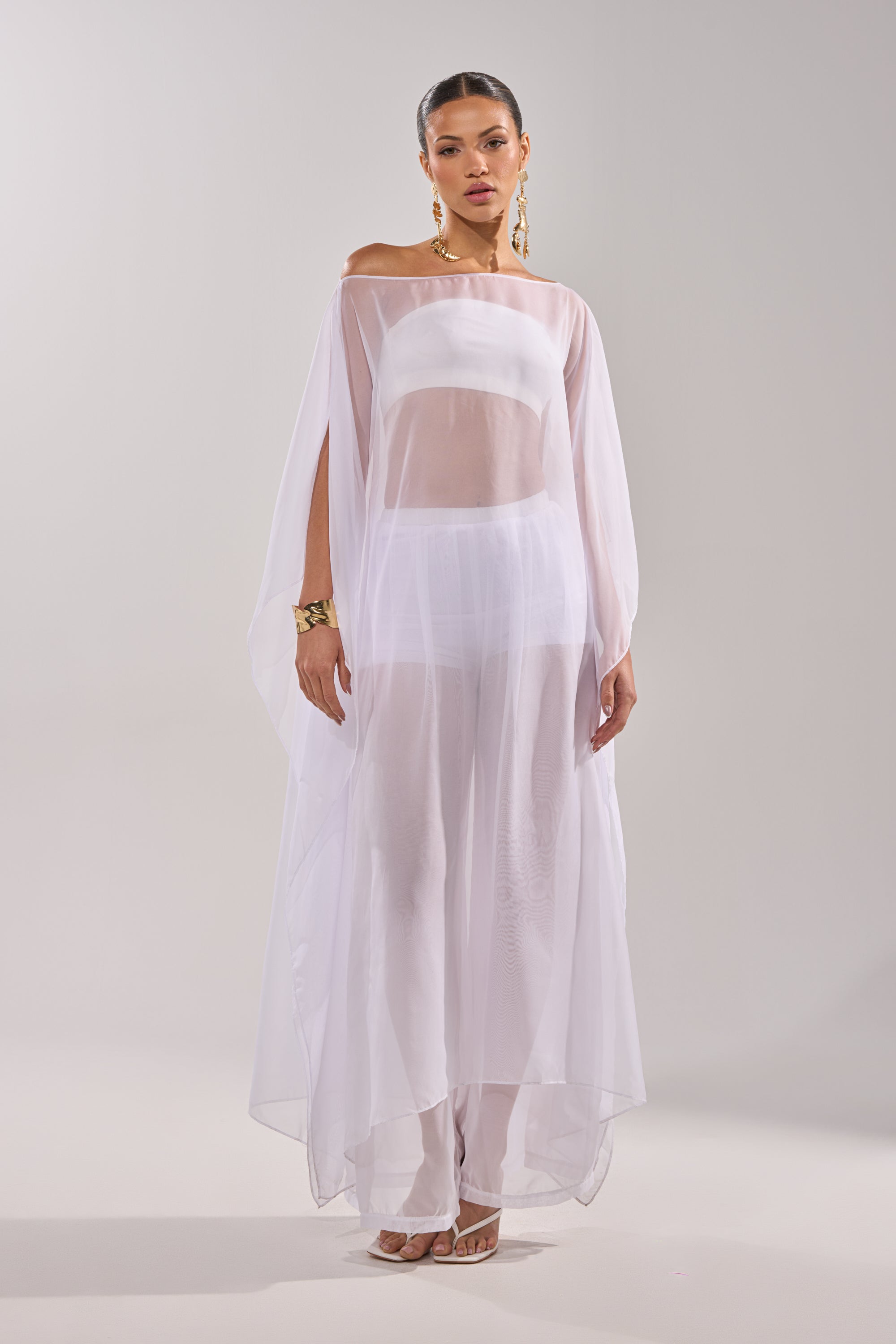 Wearing the DREAMY SHEER BLOUSE over a white dress, a woman adds an airy elegance to her look. 2