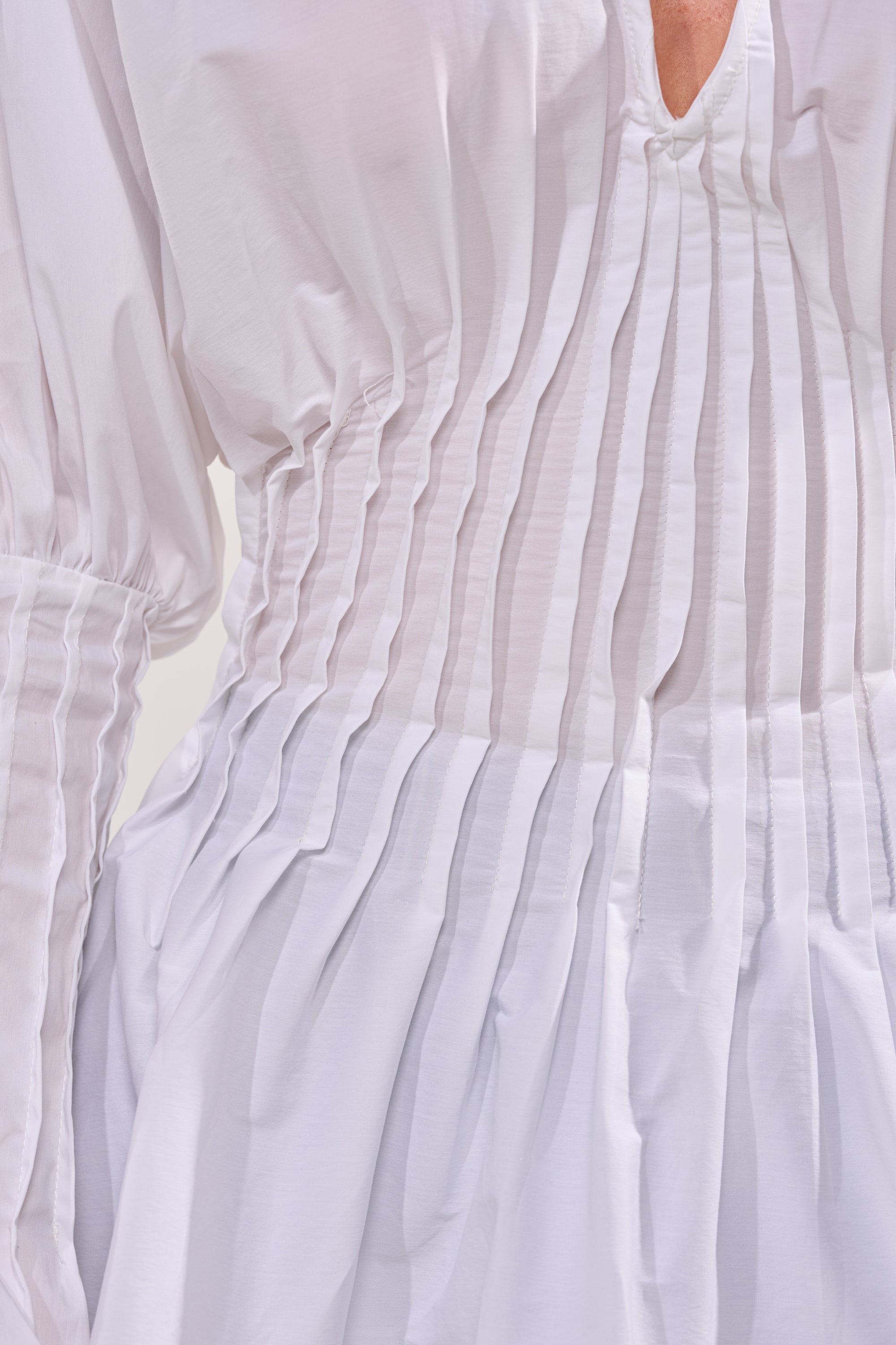 Close-up of the DONT LOOK AT ME BLOUSE: a pleated white poplin design with long balloon sleeves, vertical pleats on the bodice and sleeves, gathered skirt, and slightly sheer lightweight fabric. 5