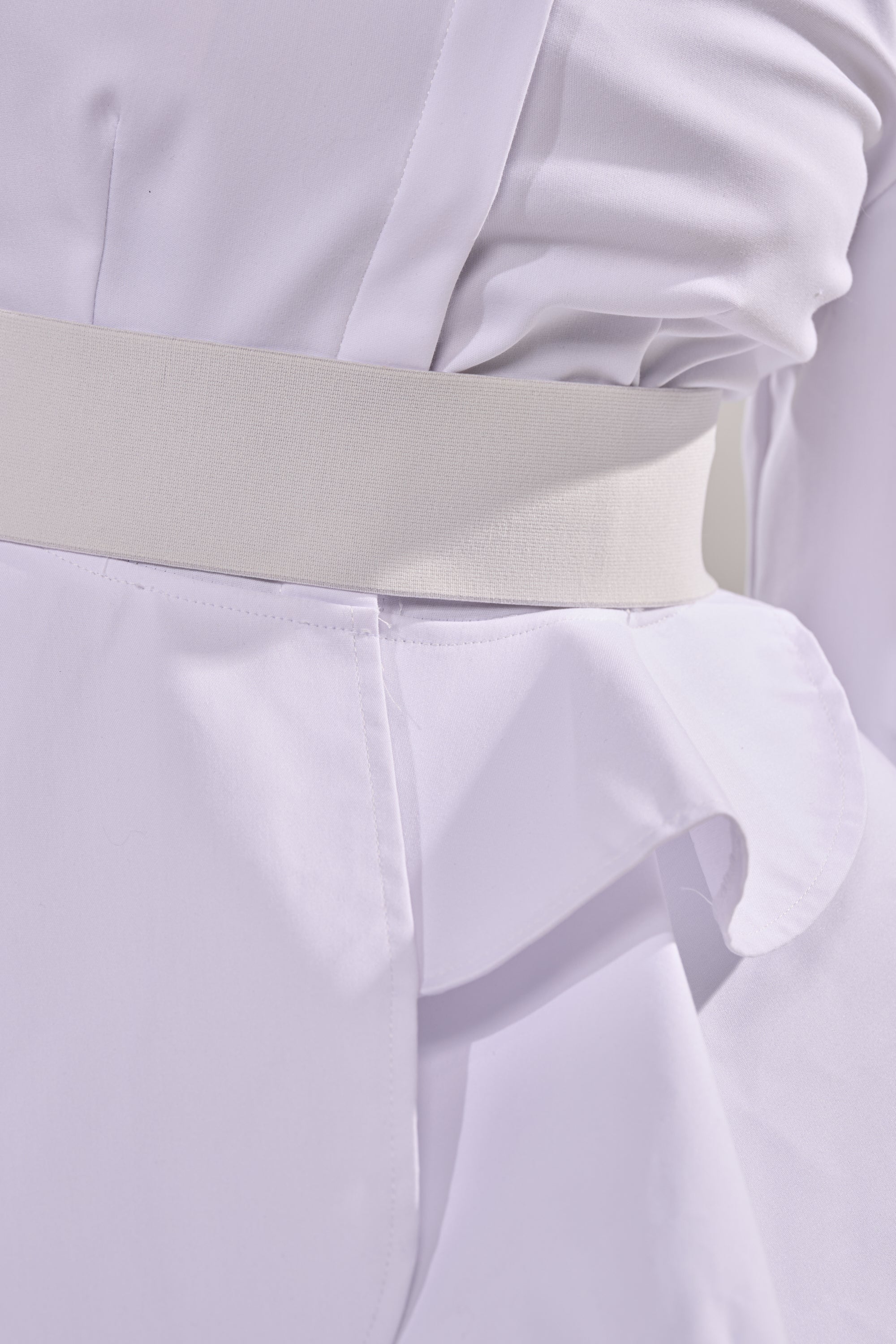 Close-up of a person wearing the ELEGANT PEPLUM BUTTON DOWN BLOUSE featuring a wide white belt, soft folds, and ruffle detail at the hip for a chic, structured look. 6