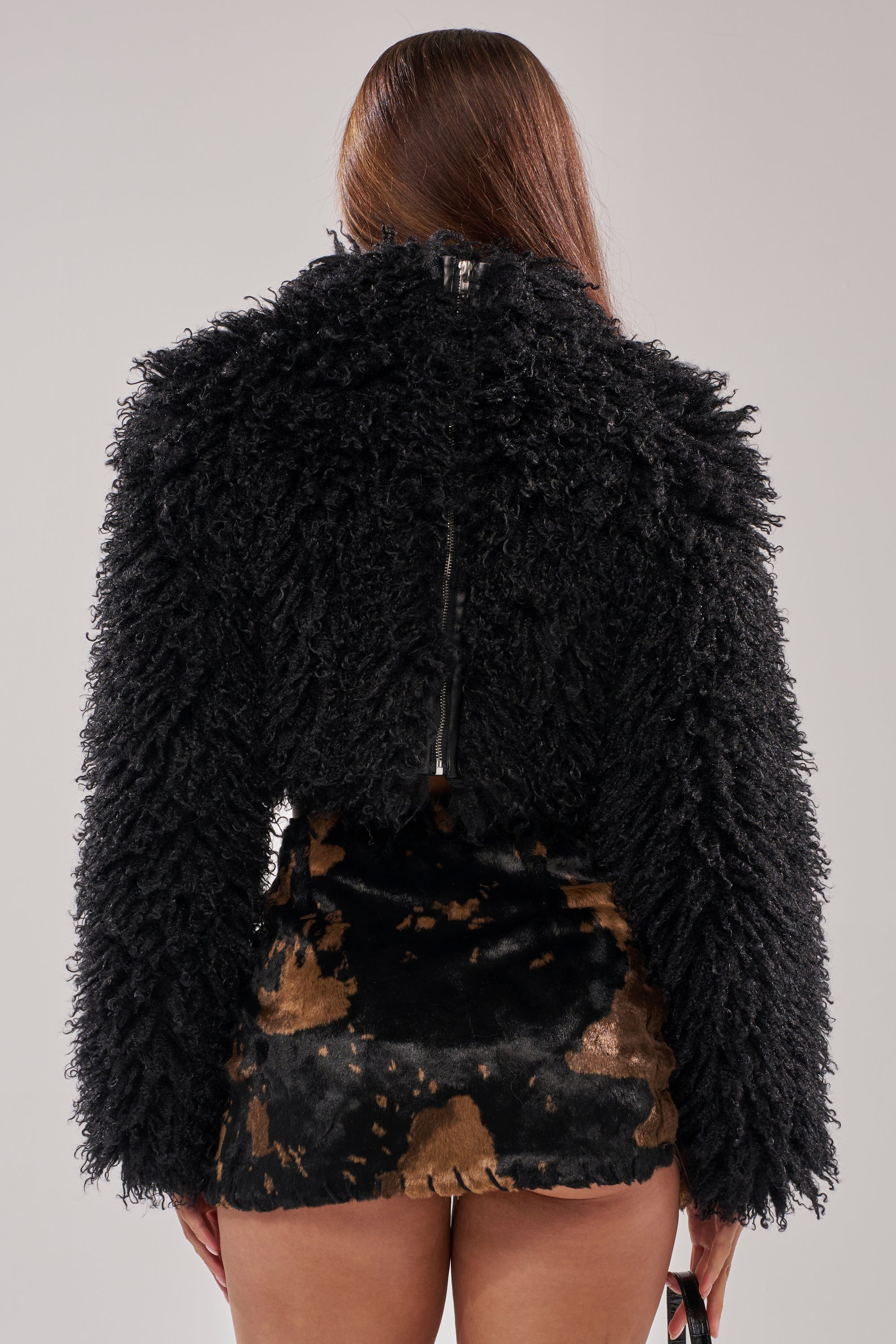 A person with long brown hair, seen from behind, wears the COOL GIRL ALERT FUR TOP and a brown and black patterned mini skirt, standing against a plain light gray background.