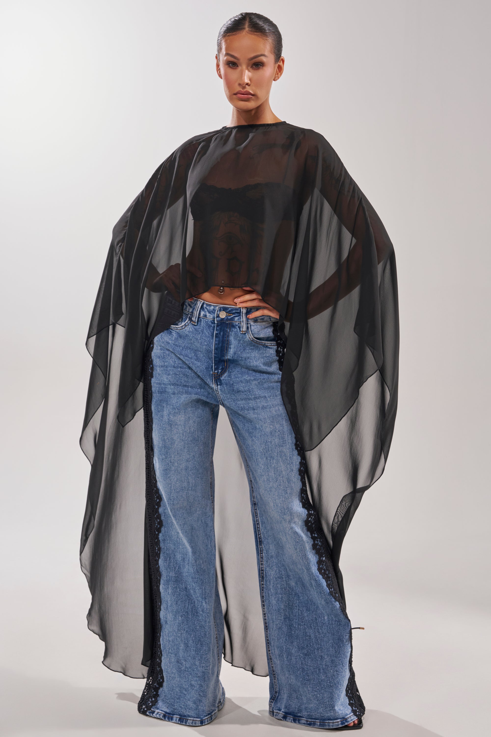 A woman wearing the COCO BLOUSE, featuring a black cape design with an asymmetrical hem. 1