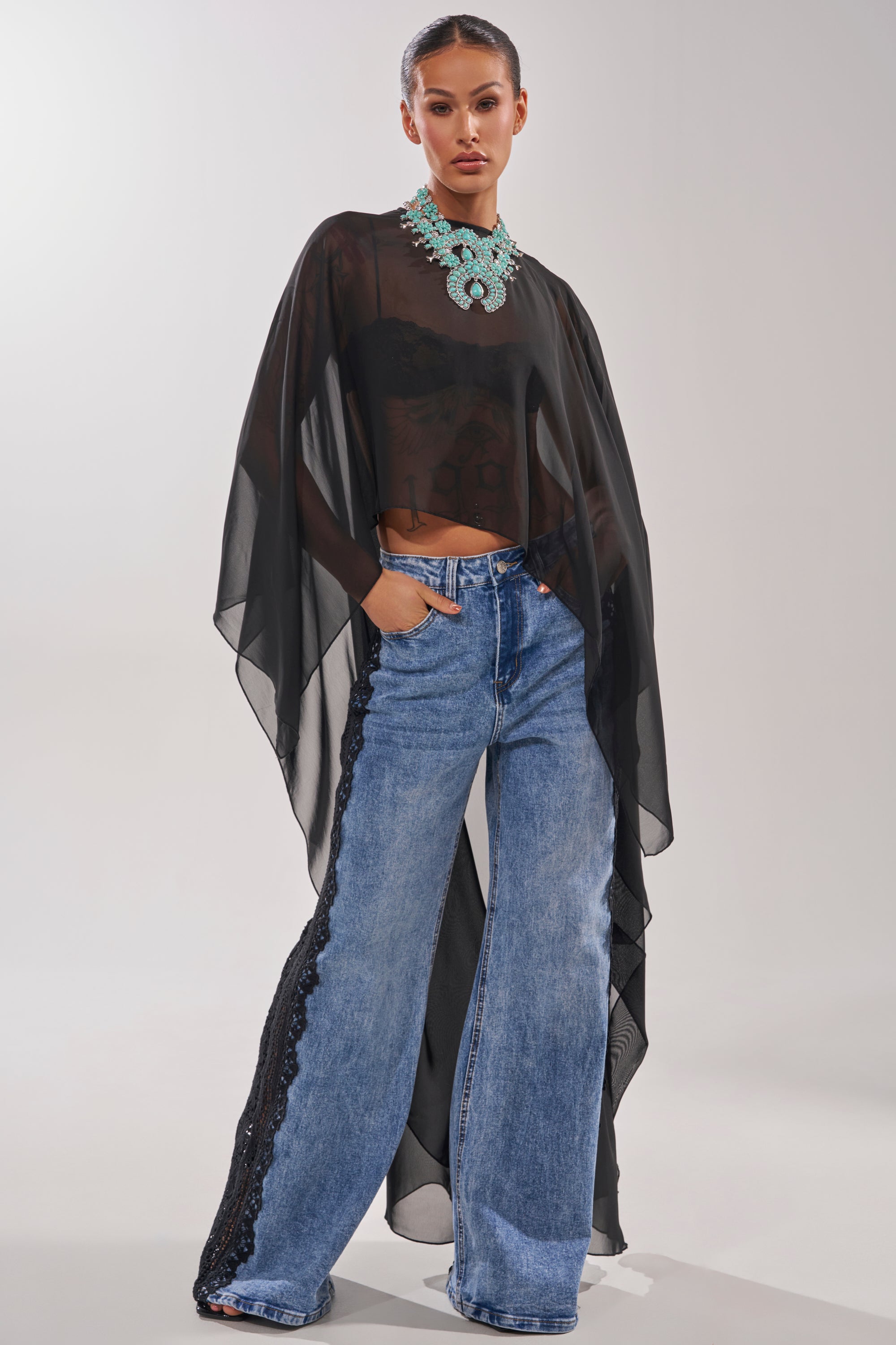 A woman wears the COCO BLOUSE, a sheer chiffon top with an asymmetrical hem, paired with blue jeans. 2