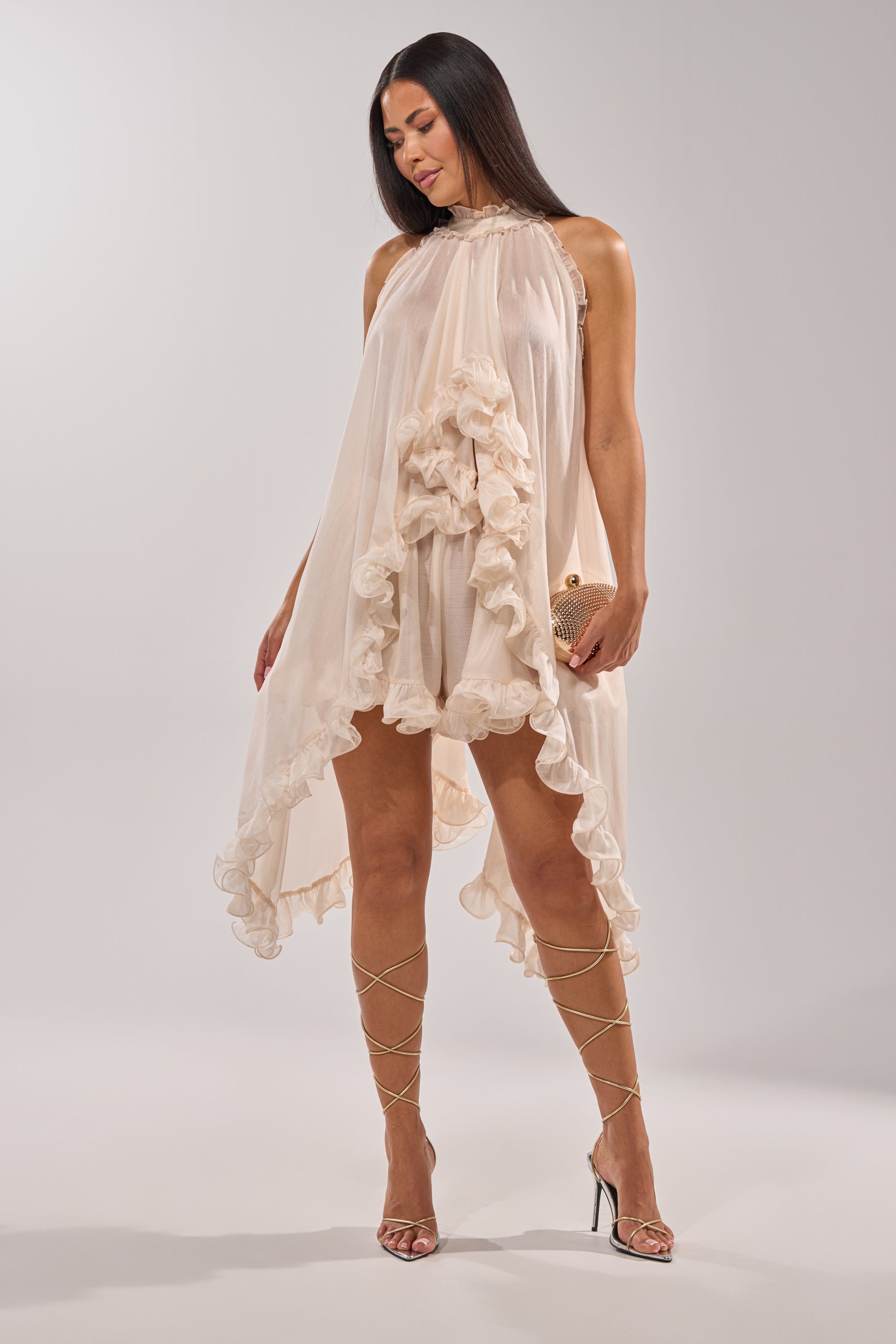 A woman makes a statement in the TALK TO ME HIGH LOW MESH BLOUSE, styled with metallic strappy high-heel sandals and a small clutch, standing against a plain light background. 4