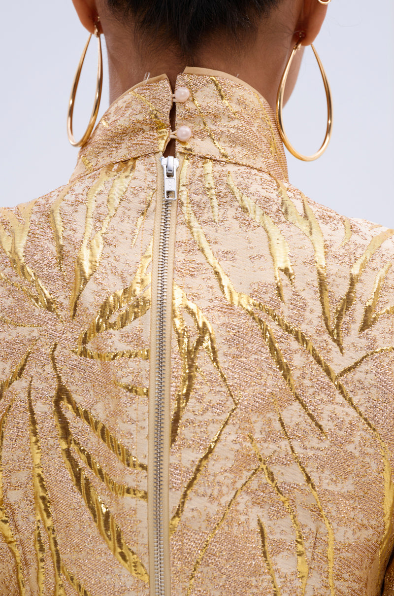 Close-up of the back of a person wearing the LANA GOLDEN BLOUSE, featuring textured gold metallic jacquard fabric, a visible zipper, and two pearl buttons at the high collar. The look is paired with large gold hoop earrings. 5
