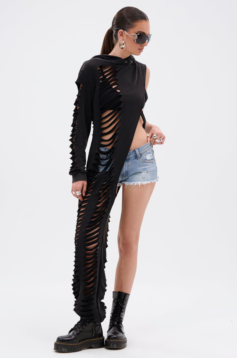 Wearing the ONE OF A KIND SWEATSHIRT with dramatic shredded cutouts, paired with sunglasses, black boots, and denim shorts, this look creates a distressed vibe against a plain white background.