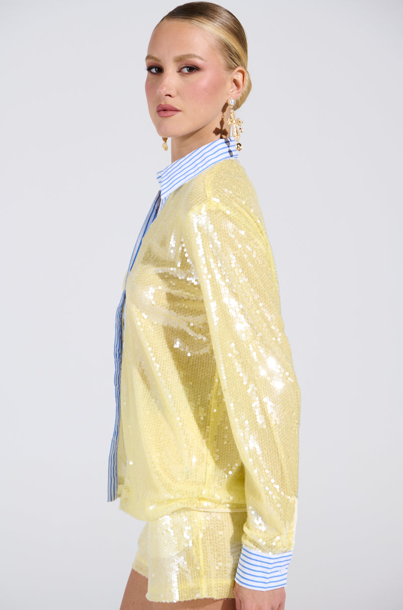 A woman poses in the DOLLY SEQUIN BUTTON DOWN TOP over a blue-and-white striped shirt with statement earrings and slicked-back hair, against a plain light background. 3