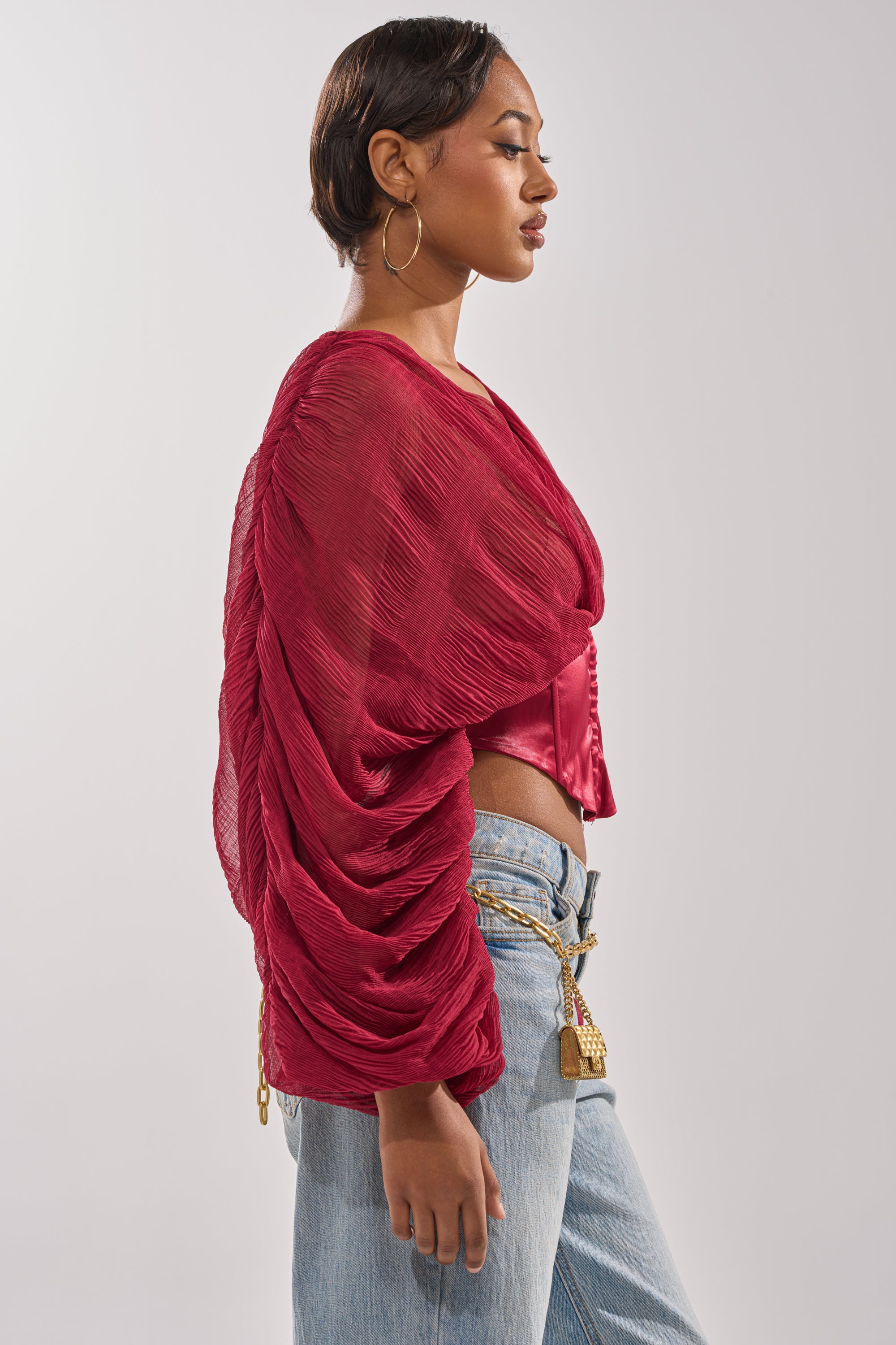 A woman in profile wears the GIRLY PLZ BLOUSE, featuring sheer chiffon and ruched balloon sleeves over a red satin corset bodice, paired with light blue jeans, large hoop earrings, and a keychain belt. 2