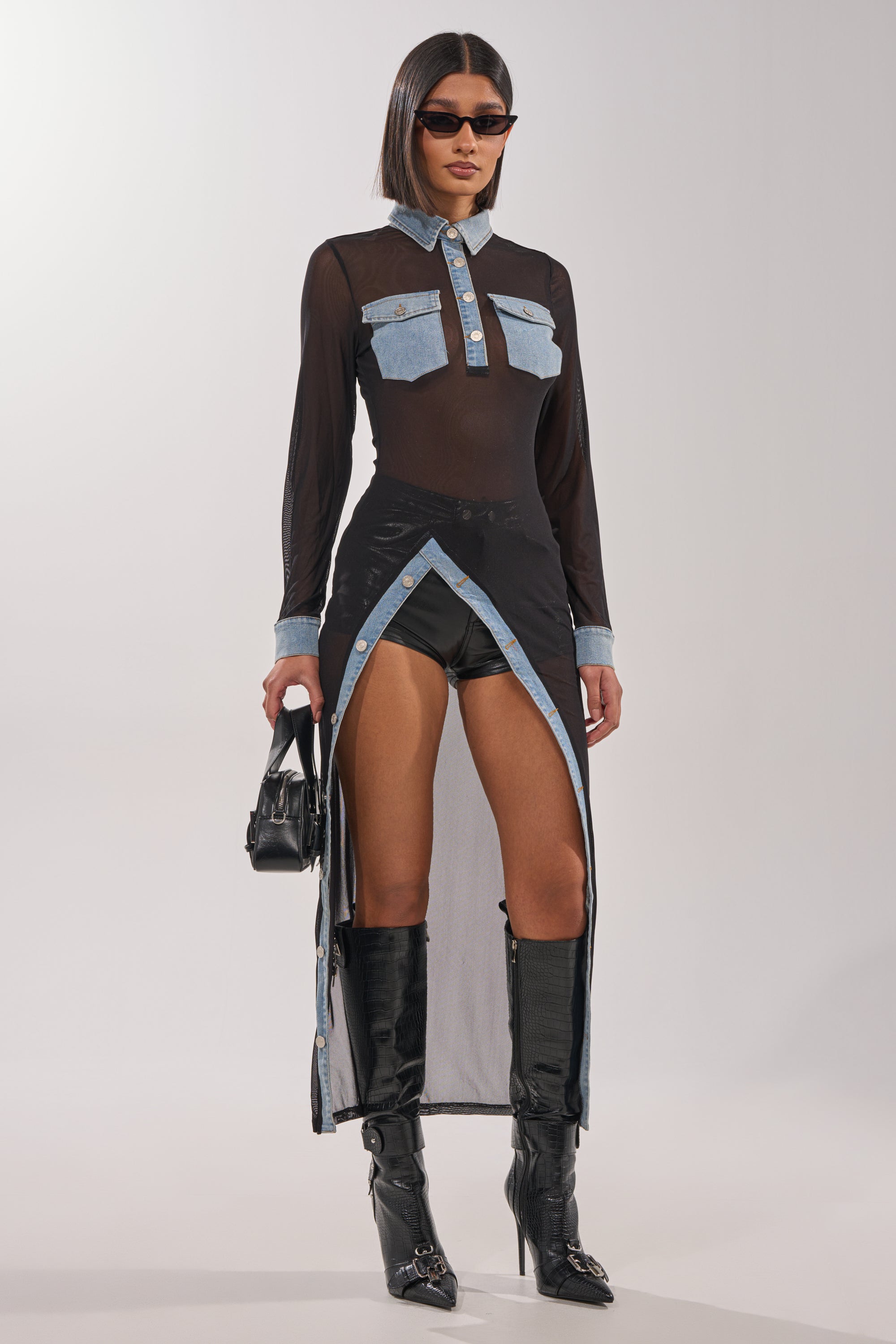 A woman wears the SABRINA LONG MESH BUTTON DOWN TOP with denim accents, styled over black shorts. She finishes her look with knee-high boots, sunglasses, and a small black handbag. 3