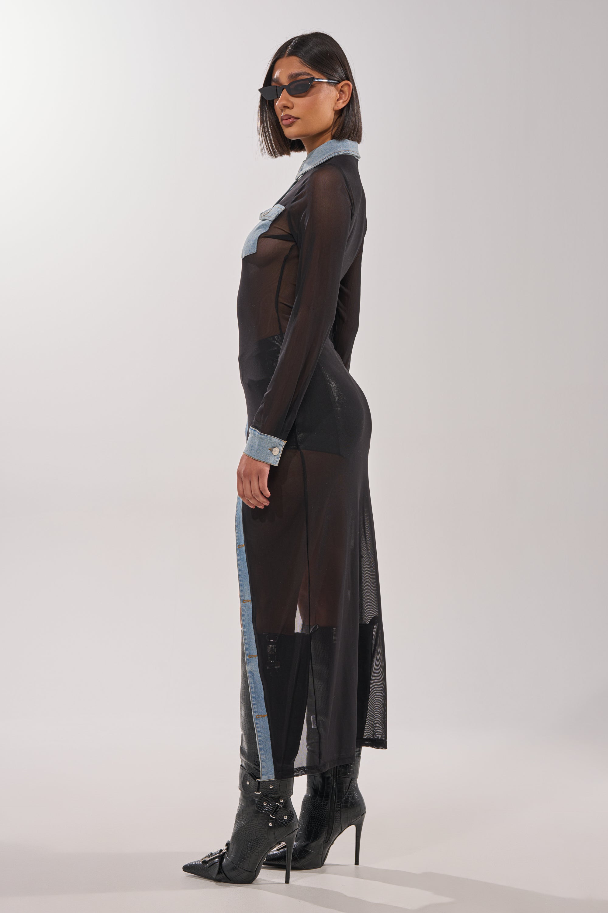 A woman in sunglasses wears the SABRINA LONG MESH BUTTON DOWN TOP with denim accents and black pointed high-heeled boots. She stands in profile against a plain light background, highlighting chic, layered styling. 4