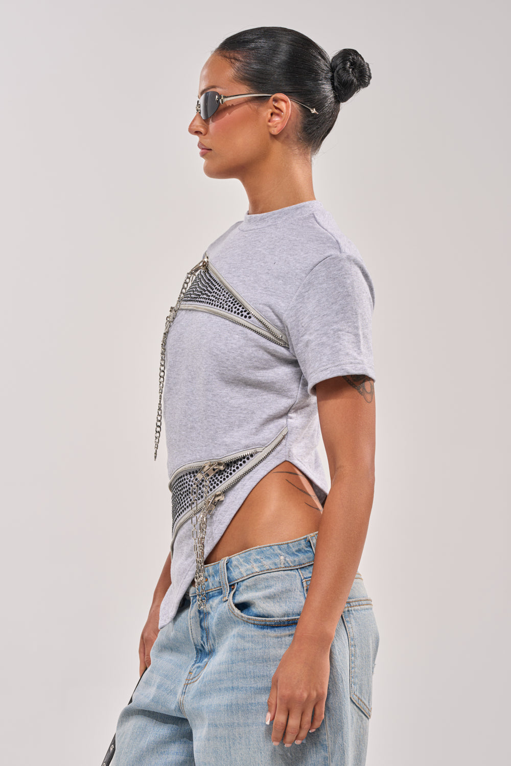 A woman with slicked-back hair in a bun and sunglasses wears the DONT MESS OVERSIZED SWEATSHIRT paired with low-rise baggy jeans. She stands in profile against a plain light background. 2