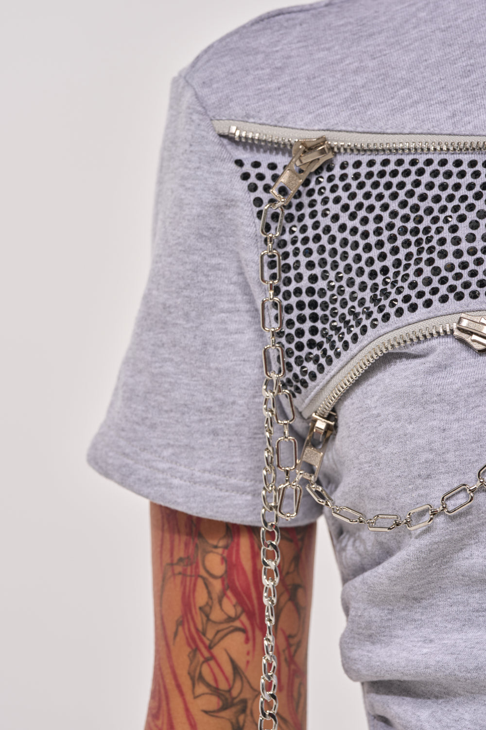 Close-up of a person wearing the DONT MESS OVERSIZED SWEATSHIRT in light gray, featuring metallic zippers, mesh panel, and a decorative silver chain. Red and black tattoos on their arm complement the streetwear short sleeve look. 8