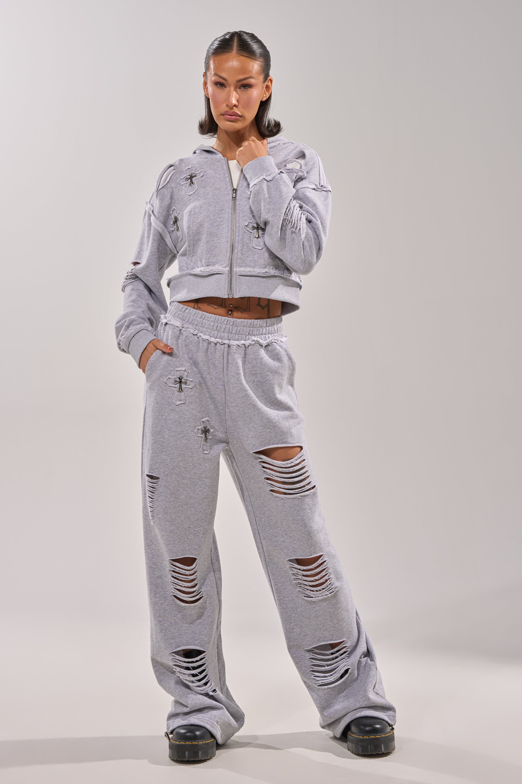 A woman stands confidently in light gray CROSSED OUT DISTRESSED WIDE LEG JOGGERS with a matching cropped zip hoodie, pairing the look with black platform shoes and sleek, straight hair. 5