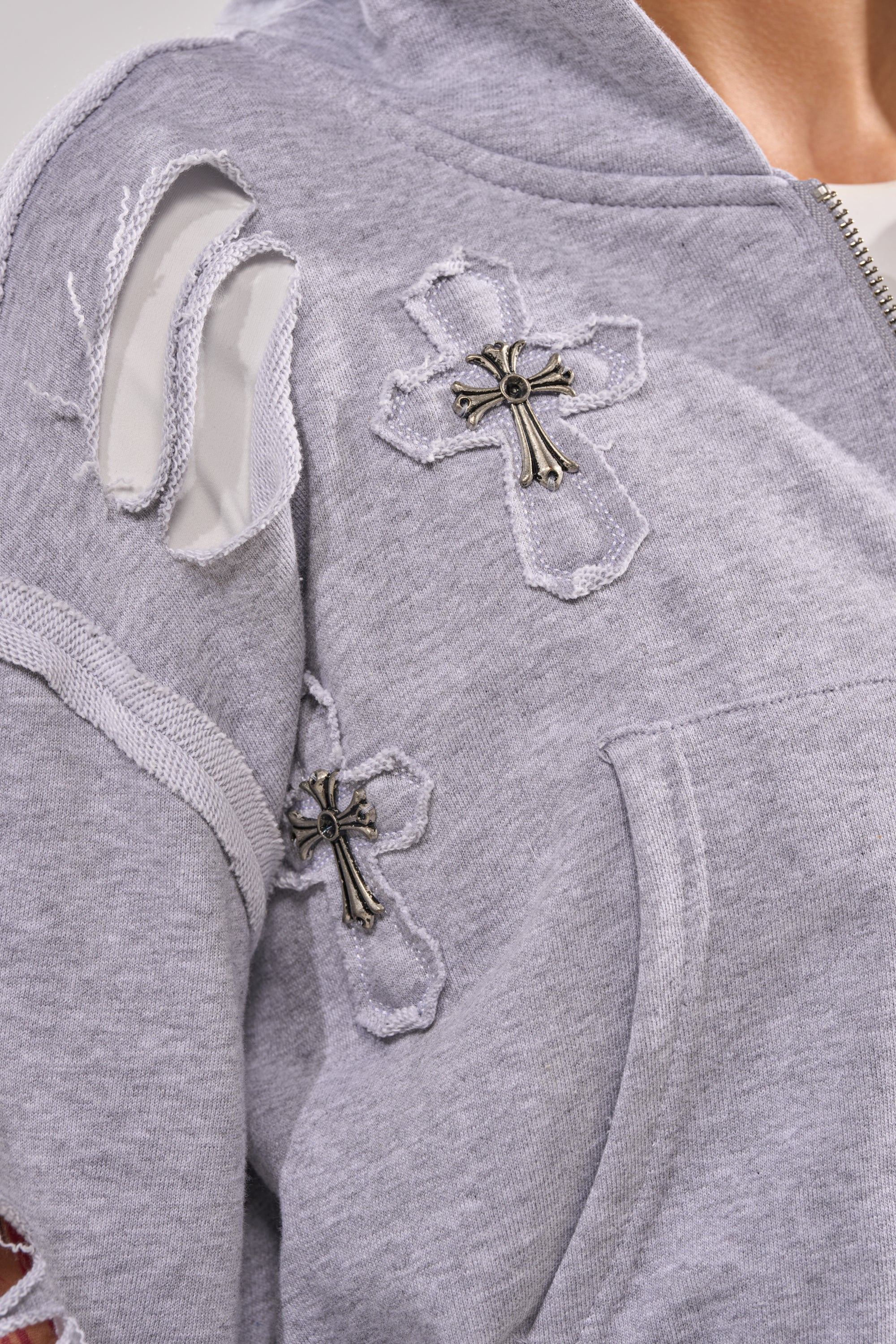 A close-up of the CROSSED OUT DISTRESSED ZIP UP SWEATSHIRT featuring frayed holes and two cross-shaped patches with metallic jeweled centers on the shoulder and chest area. 7
