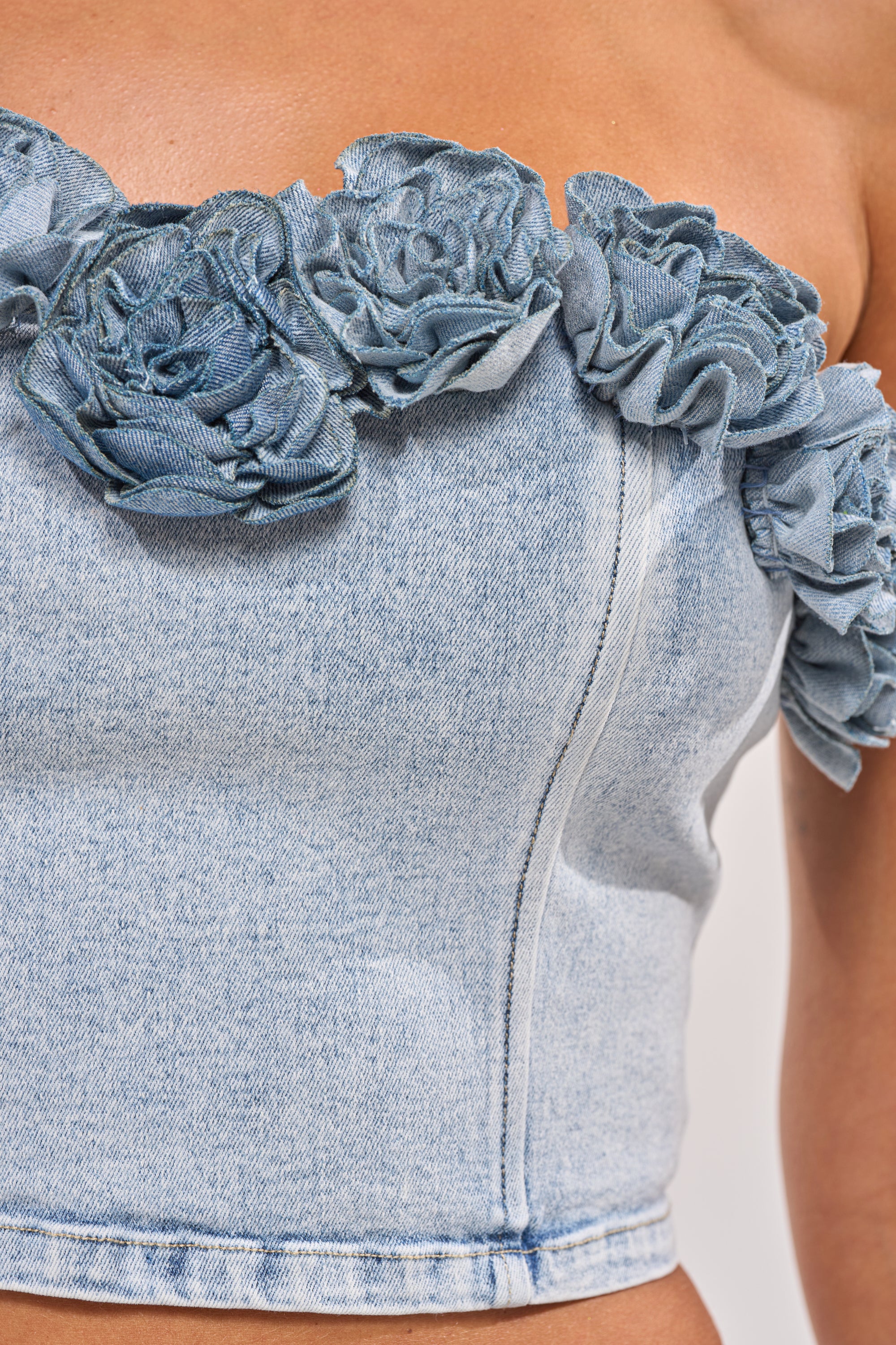 Close-up of the LOVE ME LIKE THAT FLOWER CORSET, a strapless denim top adorned with textured fabric flowers along the neckline, highlighting visible stitching and rich denim texture. 7