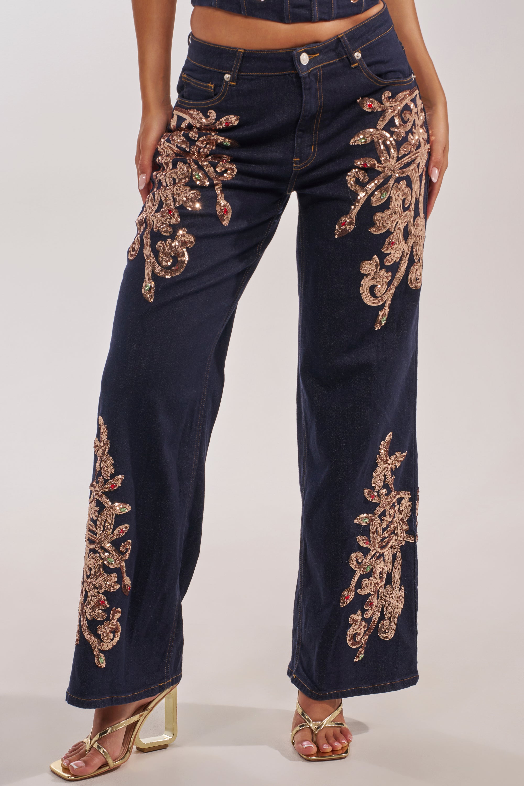 Wearing MALIBU EMBELLISHED WIDE LEG DENIM with ornate gold floral embroidery and sequins, paired with metallic gold open-toe heels. The top half of the person is not shown. 2