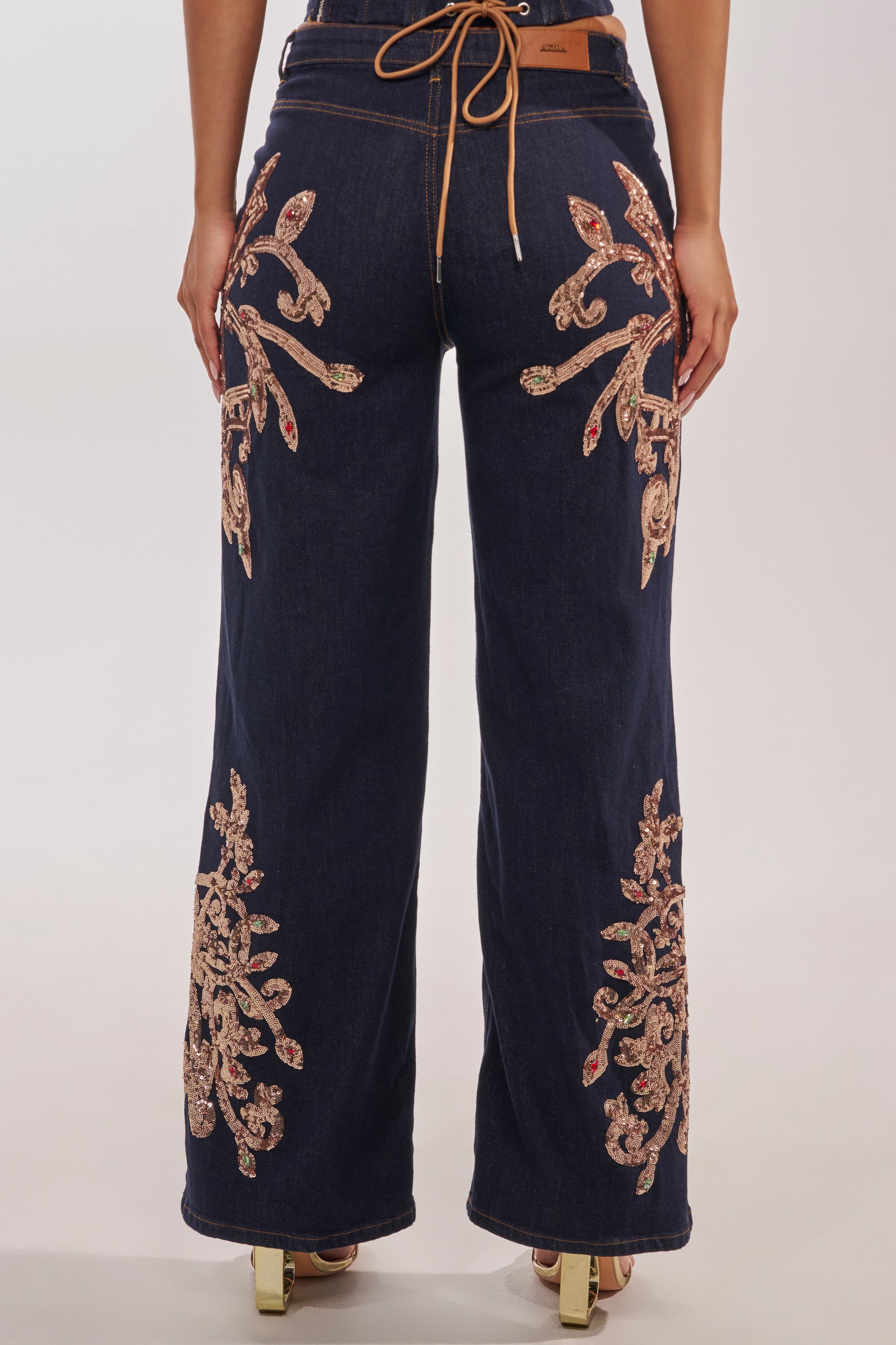 A person wearing MALIBU EMBELLISHED WIDE LEG DENIM featuring intricate gold and red embroidery on the back and lower legs, styled with tan heeled sandals. 4