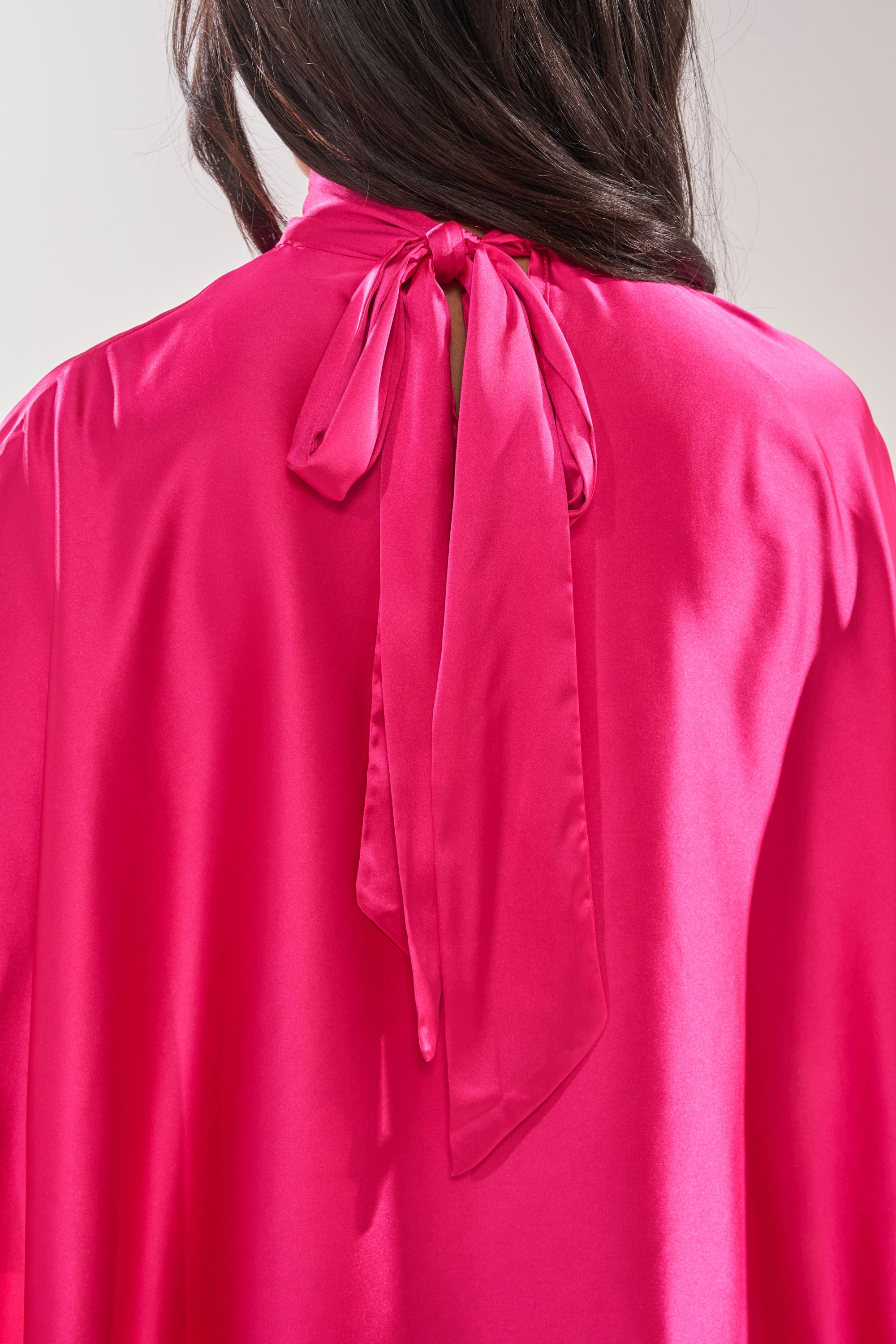 A person with long dark hair is shown from behind wearing the MAKE A MOVE BLOUSE IN FUCHSIA, featuring a bow tied at the back of the neck. 8