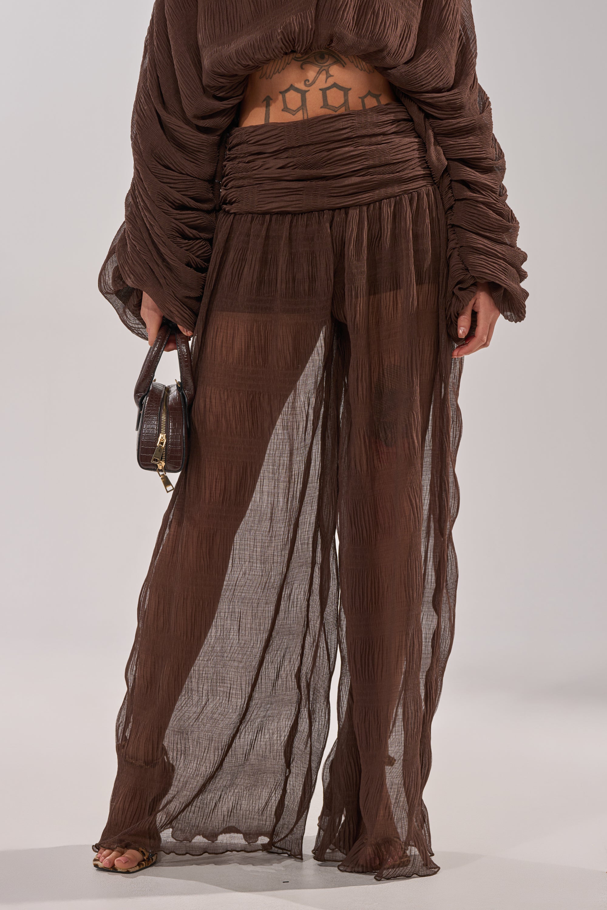 A woman wearing BABY THATS HOW I WANT IT PALAZZO PANT featuring a brown hue, high-rise smocked waistband, and sheer layered legs. 4