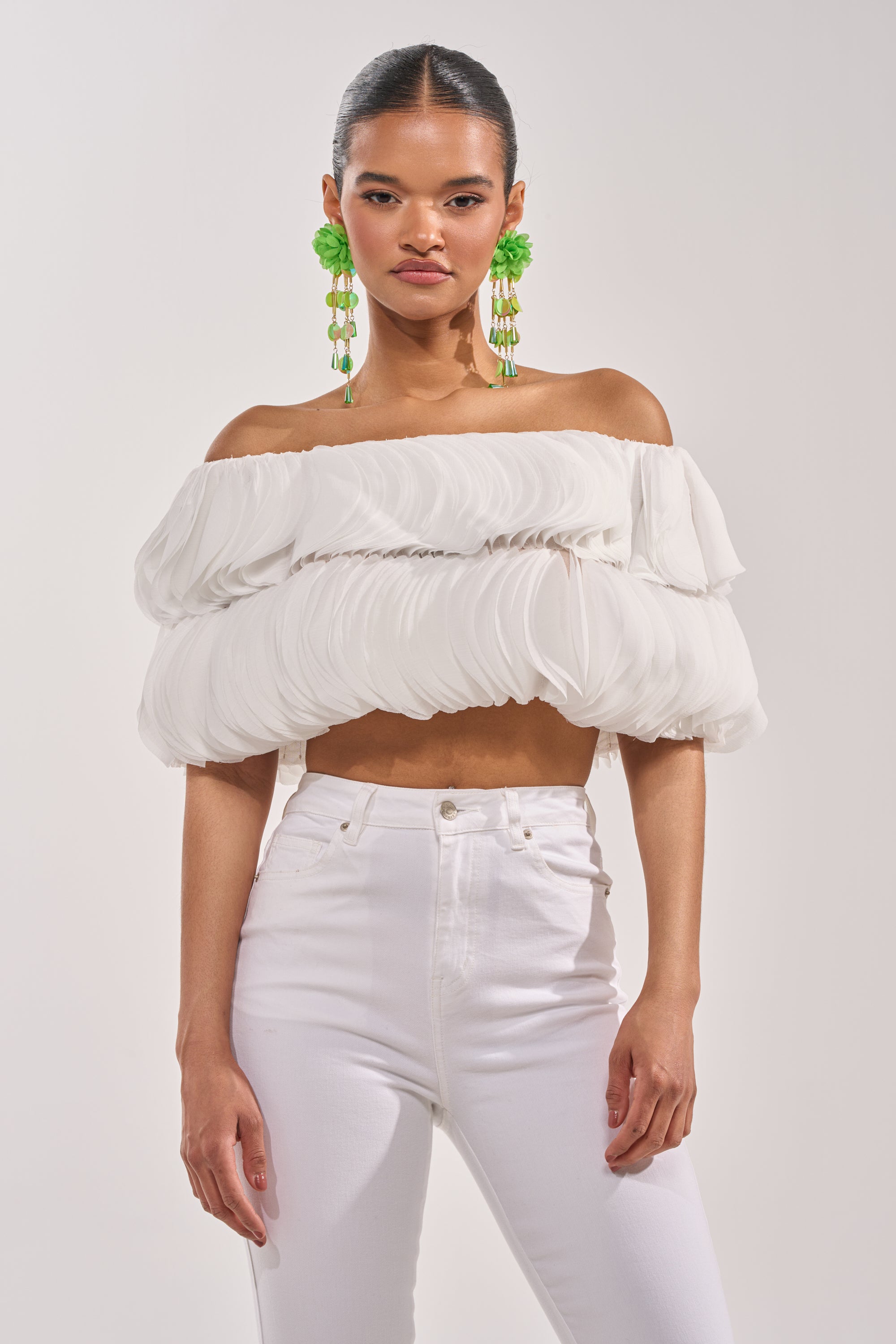Wearing the DAYDREAMER CHIFFON BLOUSE, a woman pairs it with high-waisted white pants and bold green earrings, standing confidently against a plain light background. 1