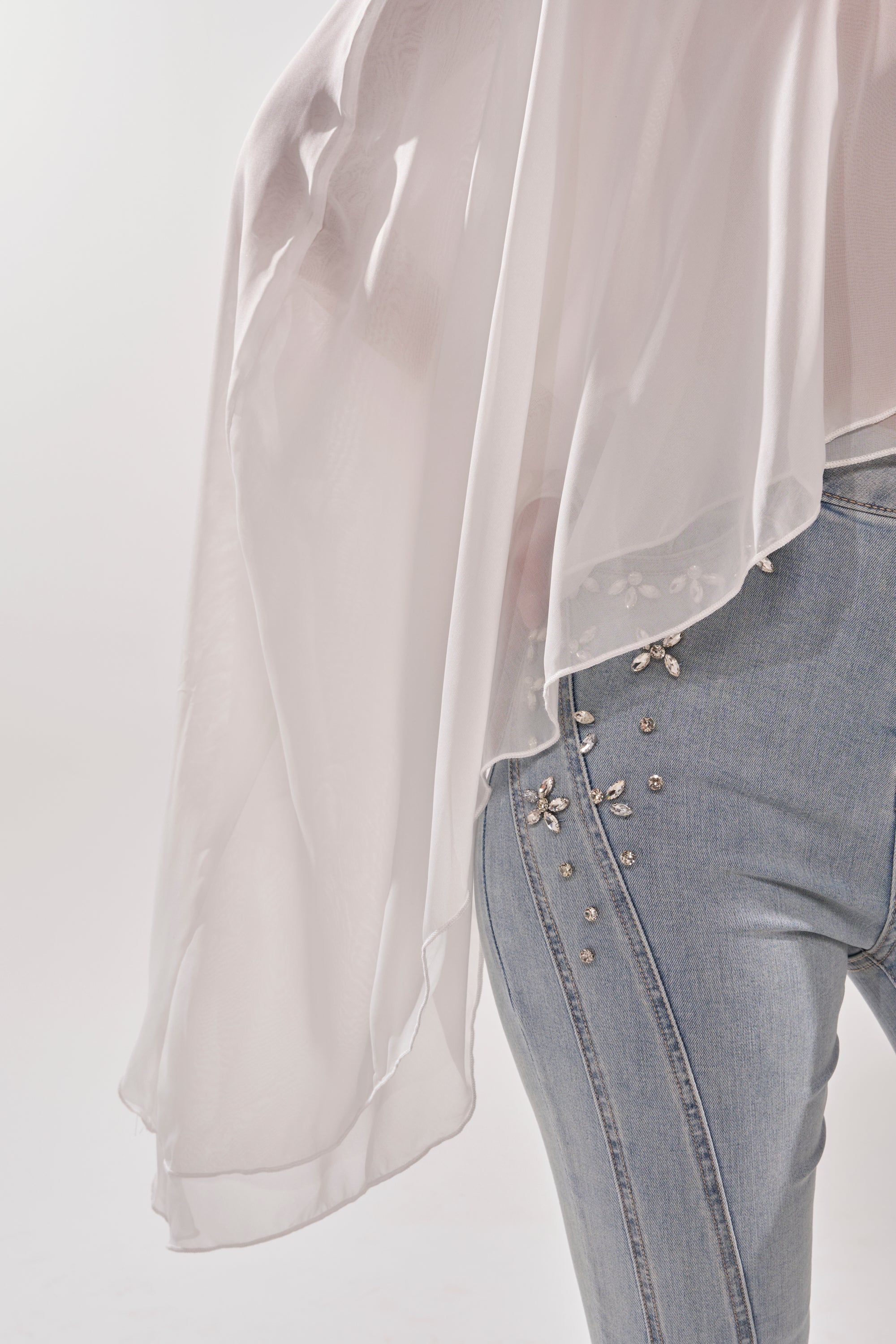 A person wears light blue jeans with rhinestones and the FOLLOW ME DRAPEY BLOUSE—a flowy white chiffon top with a mock neckline—set against a clean, minimal white background. 8