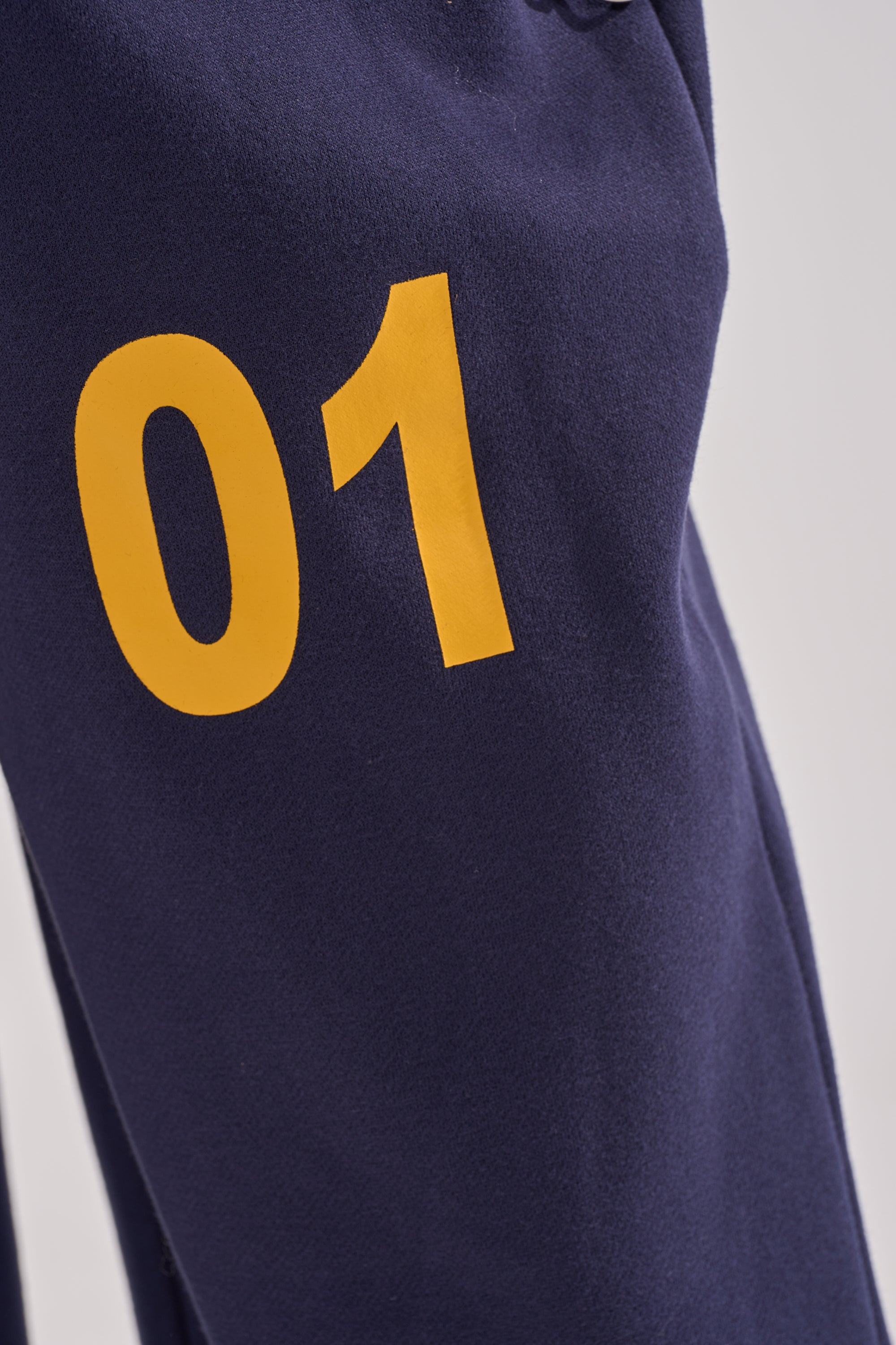 Close-up of the UNTAMED METAL RING JOGGER in navy blue fleece, featuring a yellow "01" print for a cozy and stylish look. 7