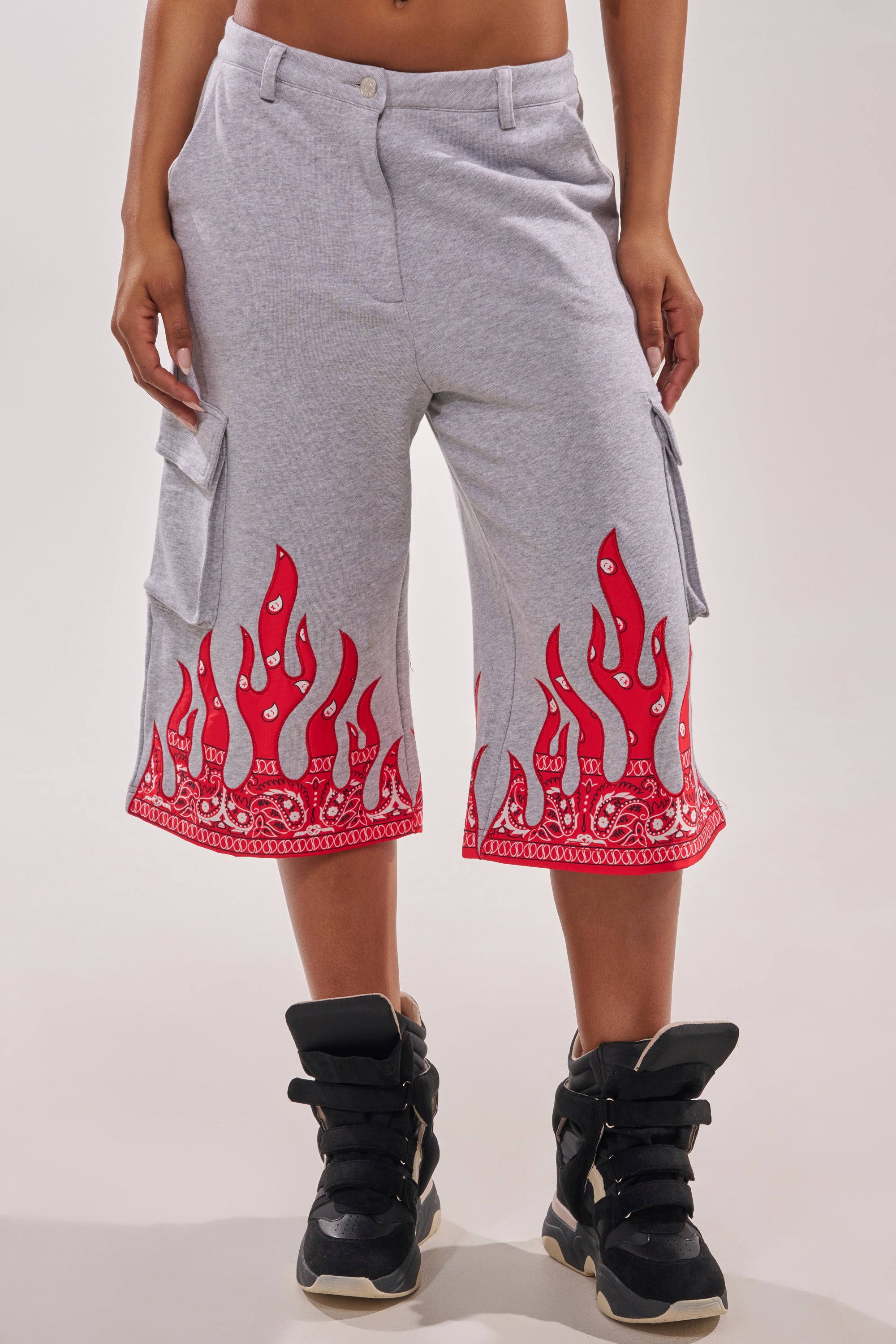 Someone wearing the FIRE TO THE FLAMES BERMUDA SHORT in light gray with red paisley flame detailing at the hem, paired with black high-top sneakers. 2