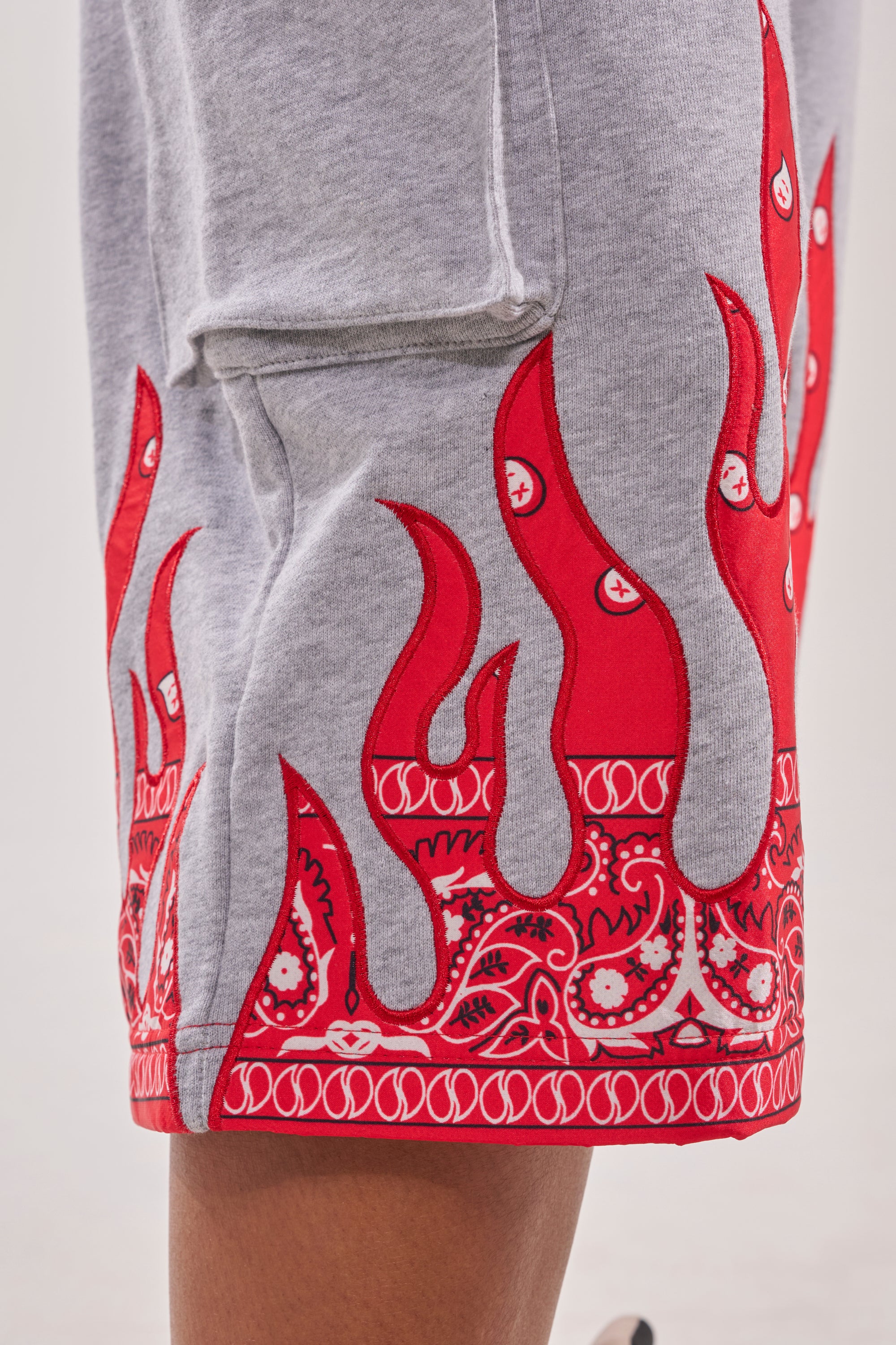 Close-up of the FIRE TO THE FLAMES BERMUDA SHORT, showcasing bold red paisley flame accents and a bandana pattern on the hem. The plain background highlights the unique cotton fabric details. 7