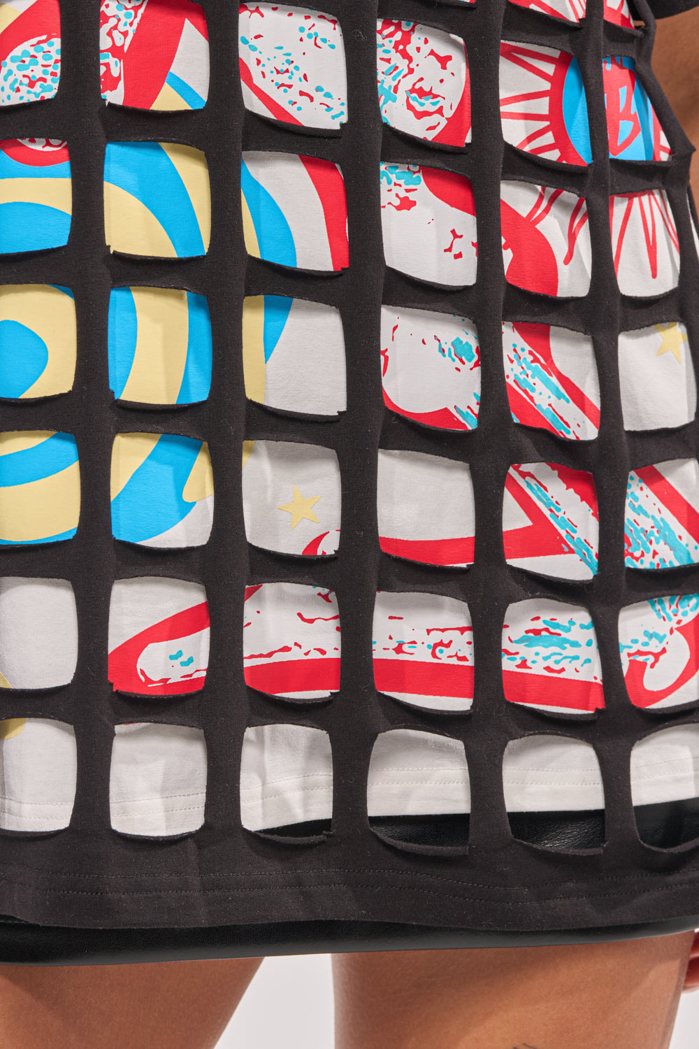 A close-up of a person wearing a black mesh grid top layered over the CHECKED OUT OVERSIZED TEE, revealing its bold, colorful abstract designs through the mesh—a vibrant, standout streetwear look. 7