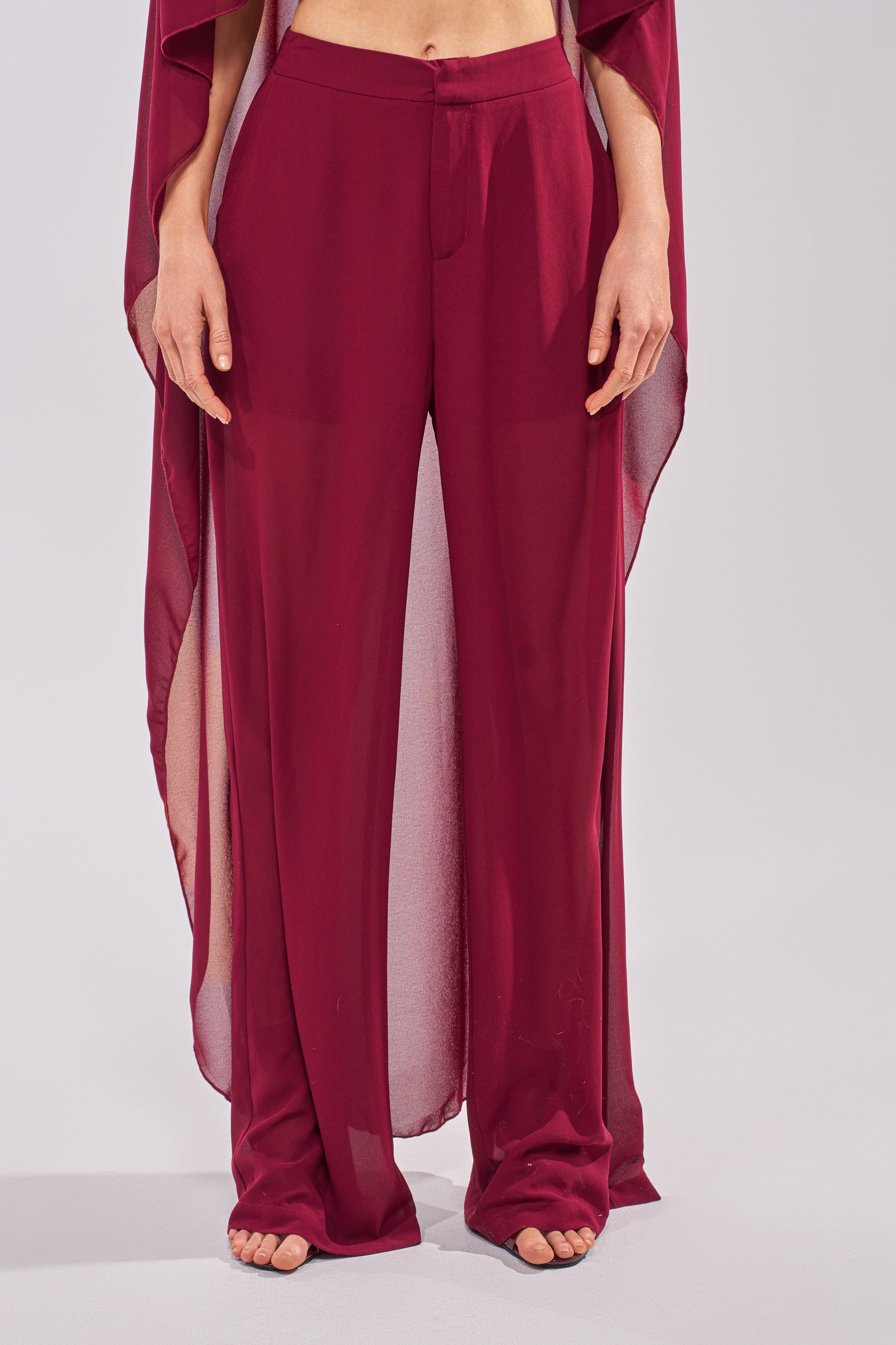 A person stands barefoot in sheer, loose-fitting COOL GIRL TROUSER chiffon pants and a matching flowing top. The high-rise trousers are partially see-through and lightweight, revealing the midriff against a plain, light background. 0