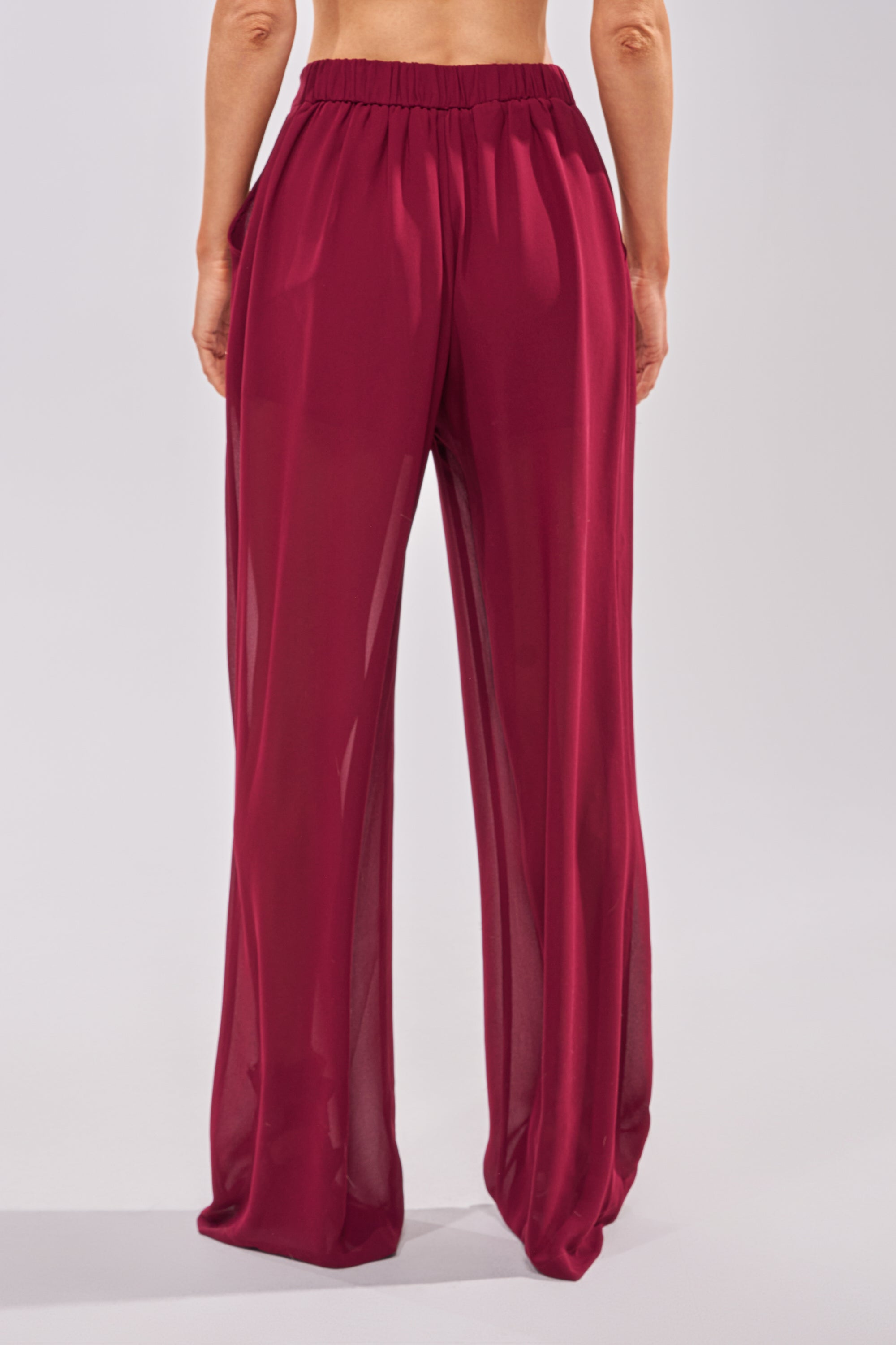A person wearing the COOL GIRL TROUSER—flowy, high-waisted maroon chiffon wide-leg pants—stands facing away from the camera against a plain light background. 2