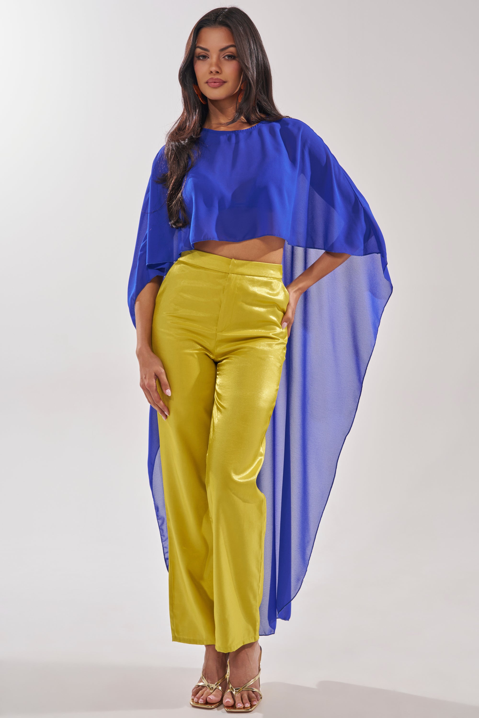A woman with long dark hair wears the COOL GIRL CHIFFON BLOUSE IN ROYAL BLUE, styled with yellow high-waisted pants and gold sandals, posing against a plain light background. 4