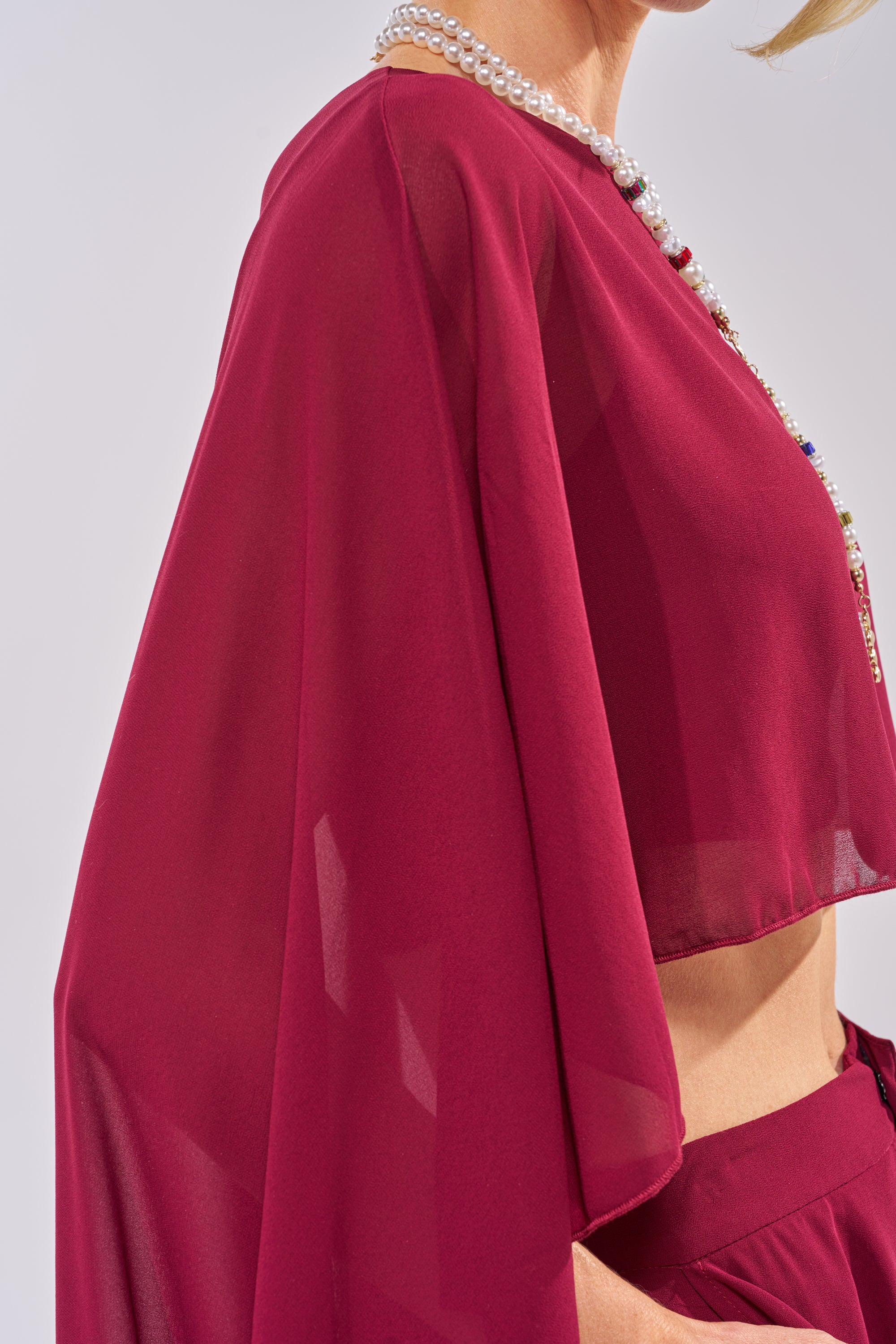 A person models the COOL GIRL CHIFFON BLOUSE IN BURGUNDY, paired with matching pants and a pearl necklace. The photo, cropped to the torso and part of the face, is set against a neutral background. 5