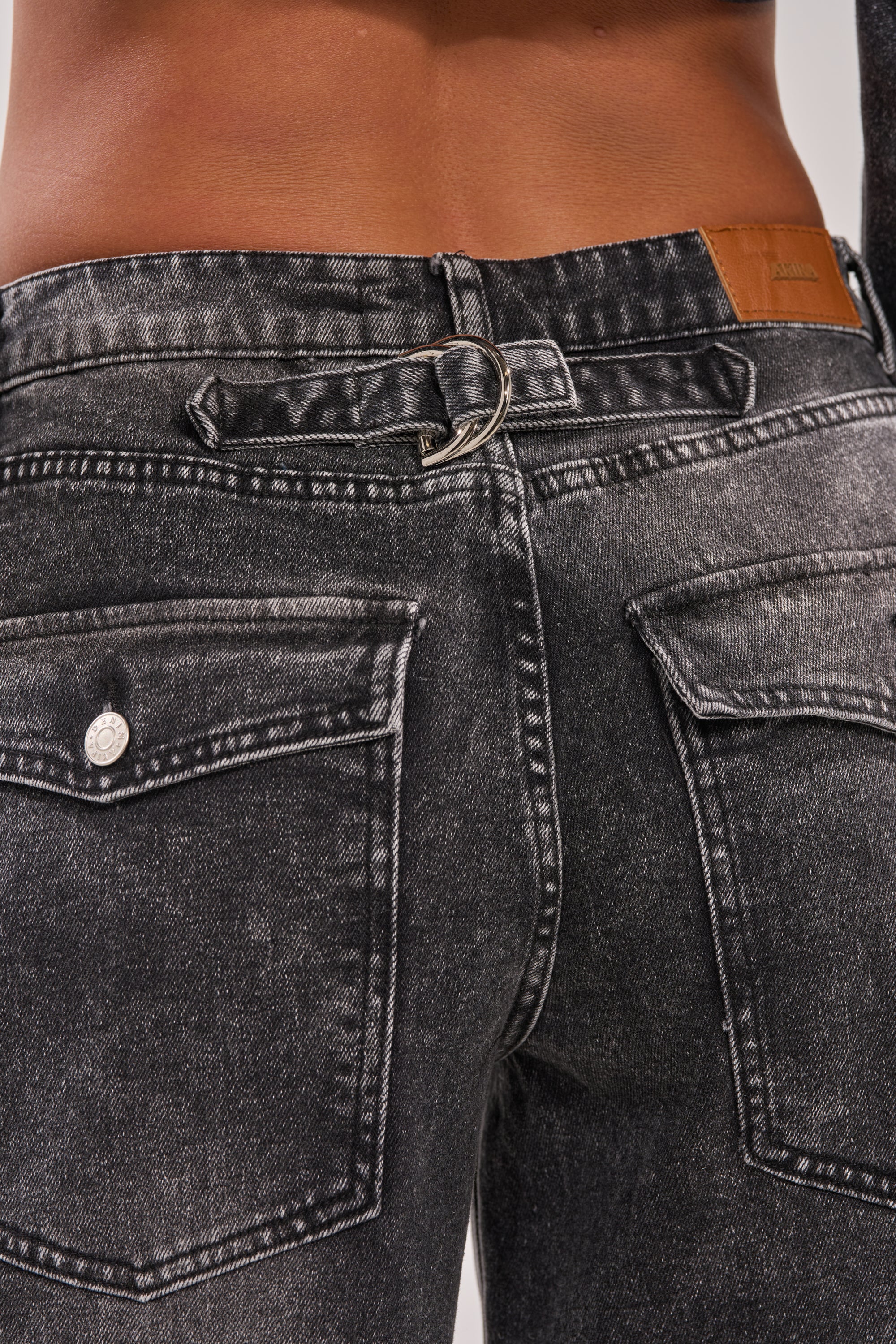 Close-up of the back of a person wearing the IN MY OWN WORLD BERMUDA SHORT, featuring black denim, large pockets, a leather patch on the high-rise waist, and a metal key ring on a belt loop. 9